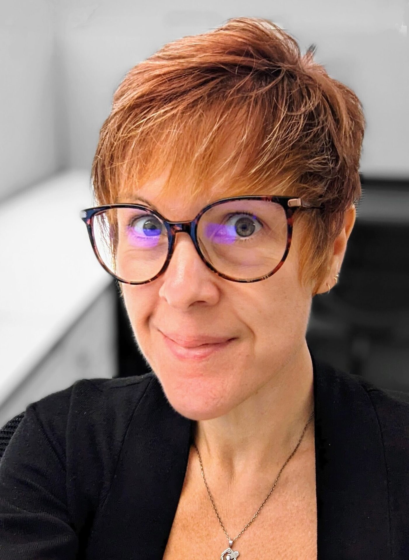 Smiling woman with short, reddish-brown hair and glasses, looking at the viewer.