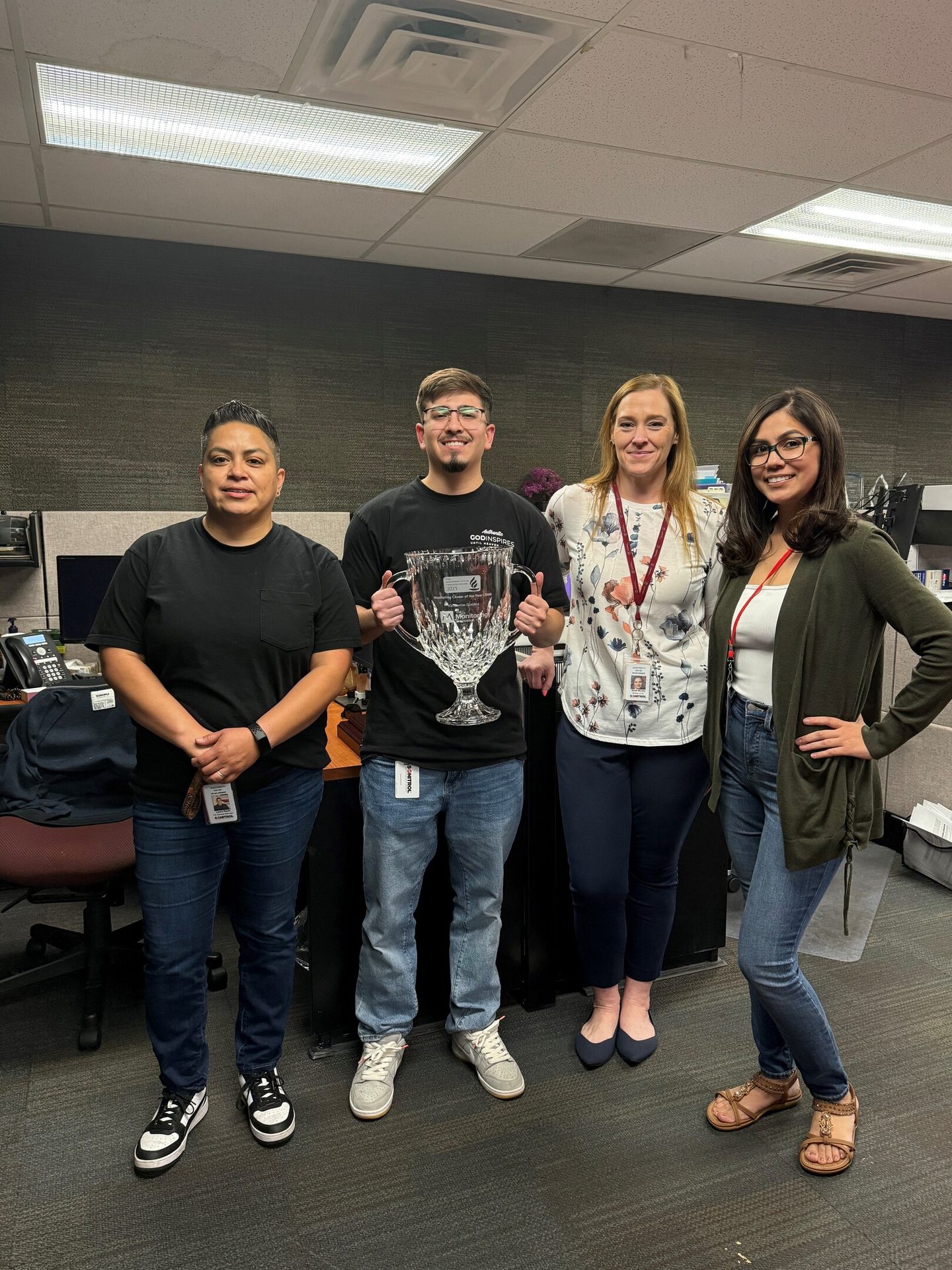 Four colleagues in an office, one holding a large trophy.