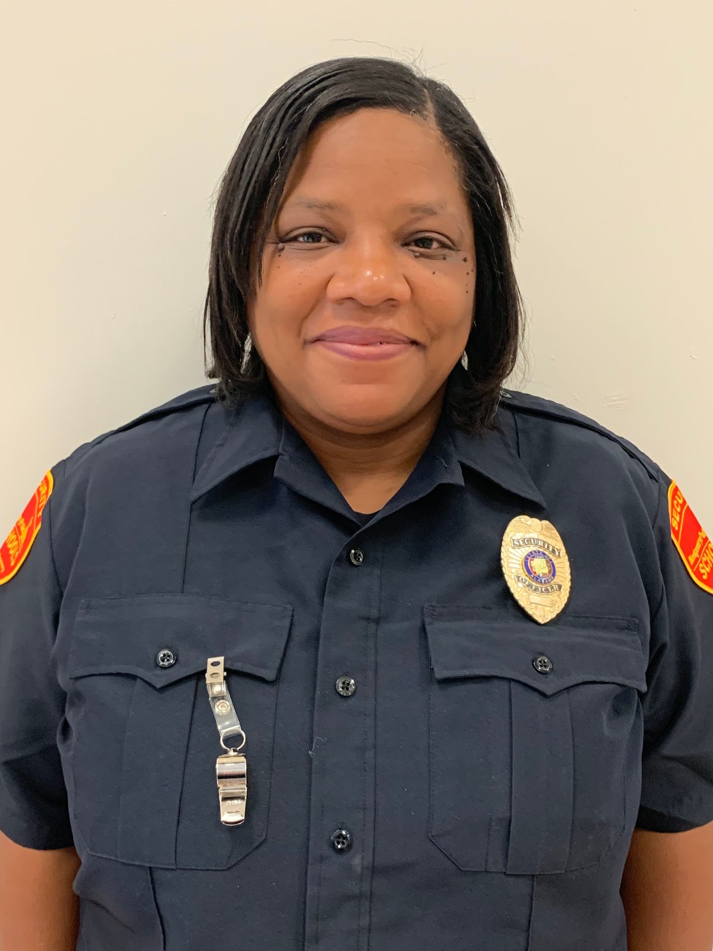 Security officer in dark uniform with badge, shoulder patches, and whistle.