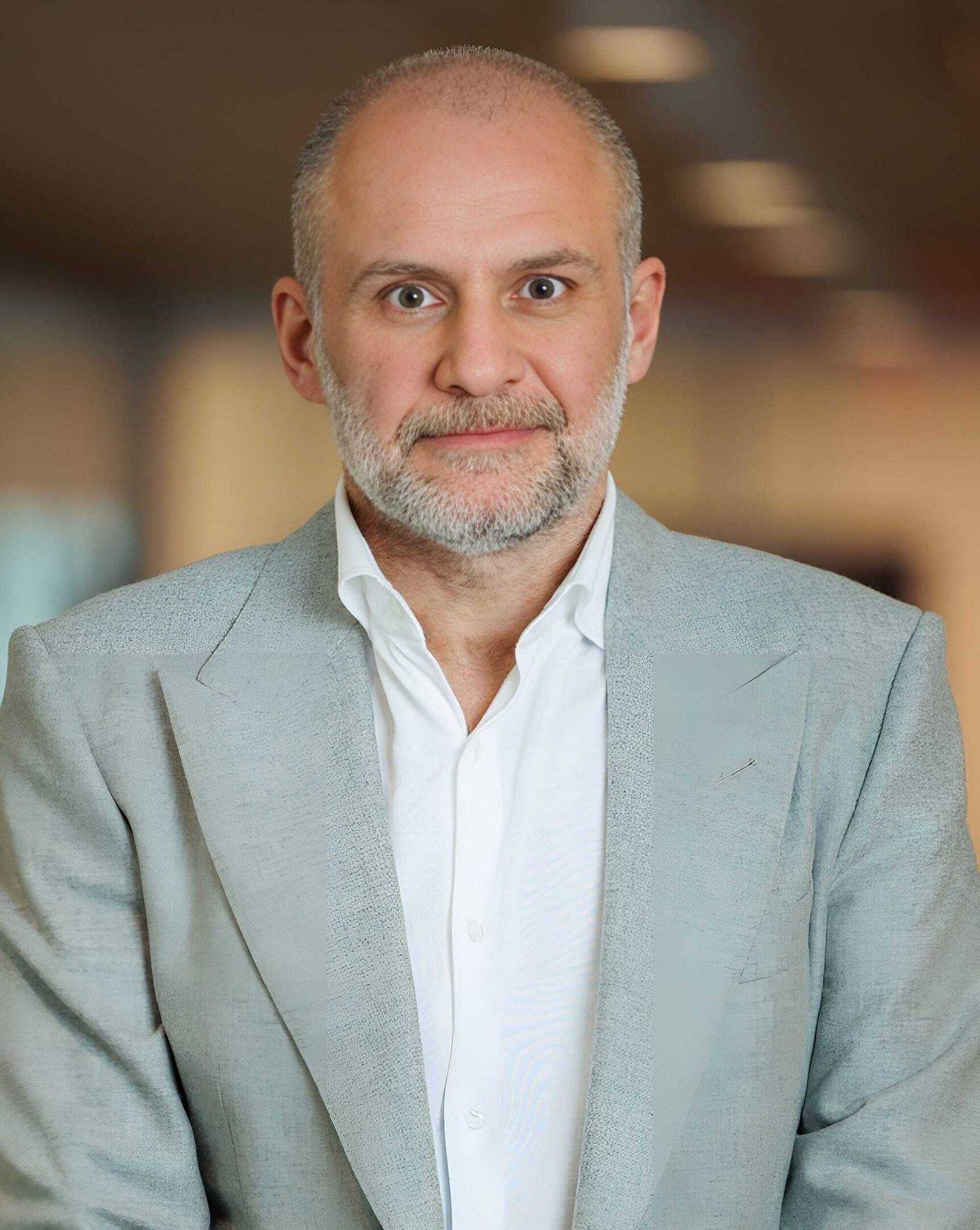 Bald, bearded man in light gray blazer and white shirt, looking directly at camera.