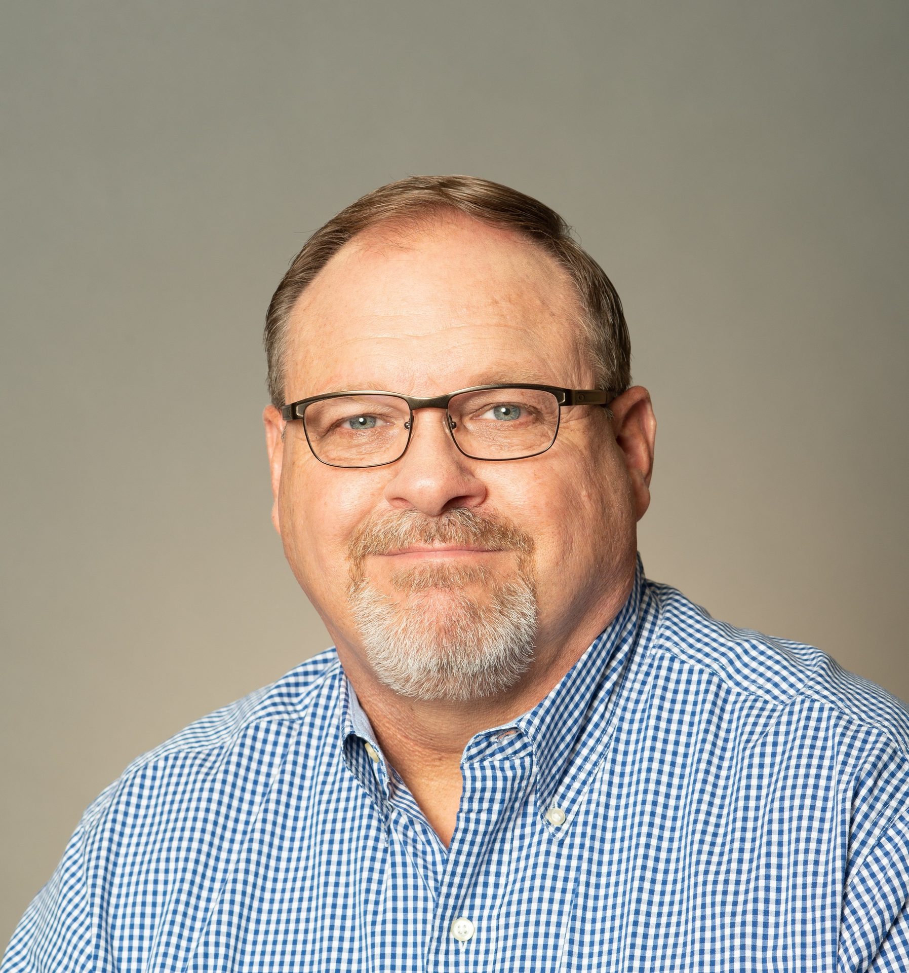 Smiling man with glasses, goatee, and blue checkered shirt.