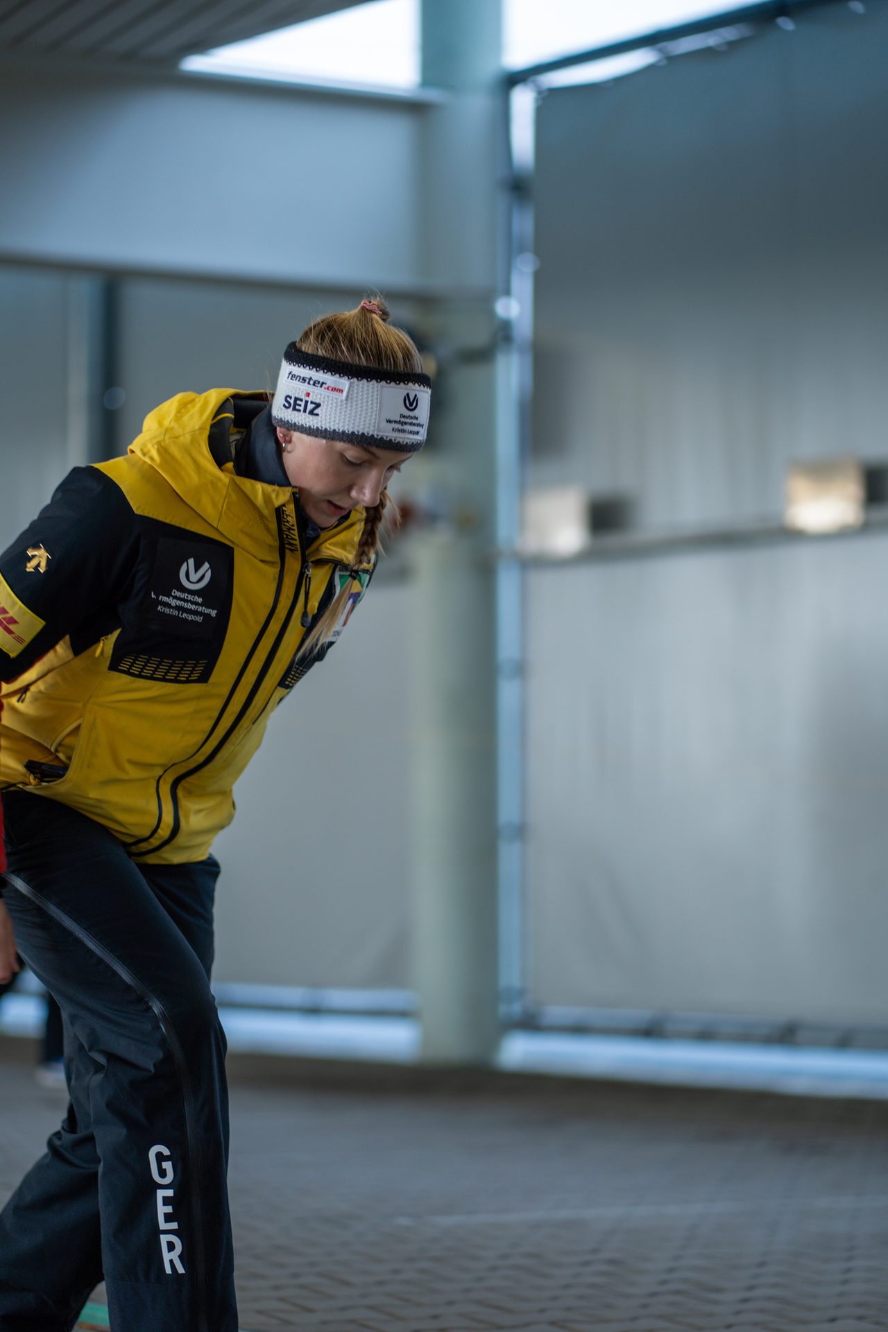 Female athlete in a yellow and black jacket and black pants with "GER," bending forward.