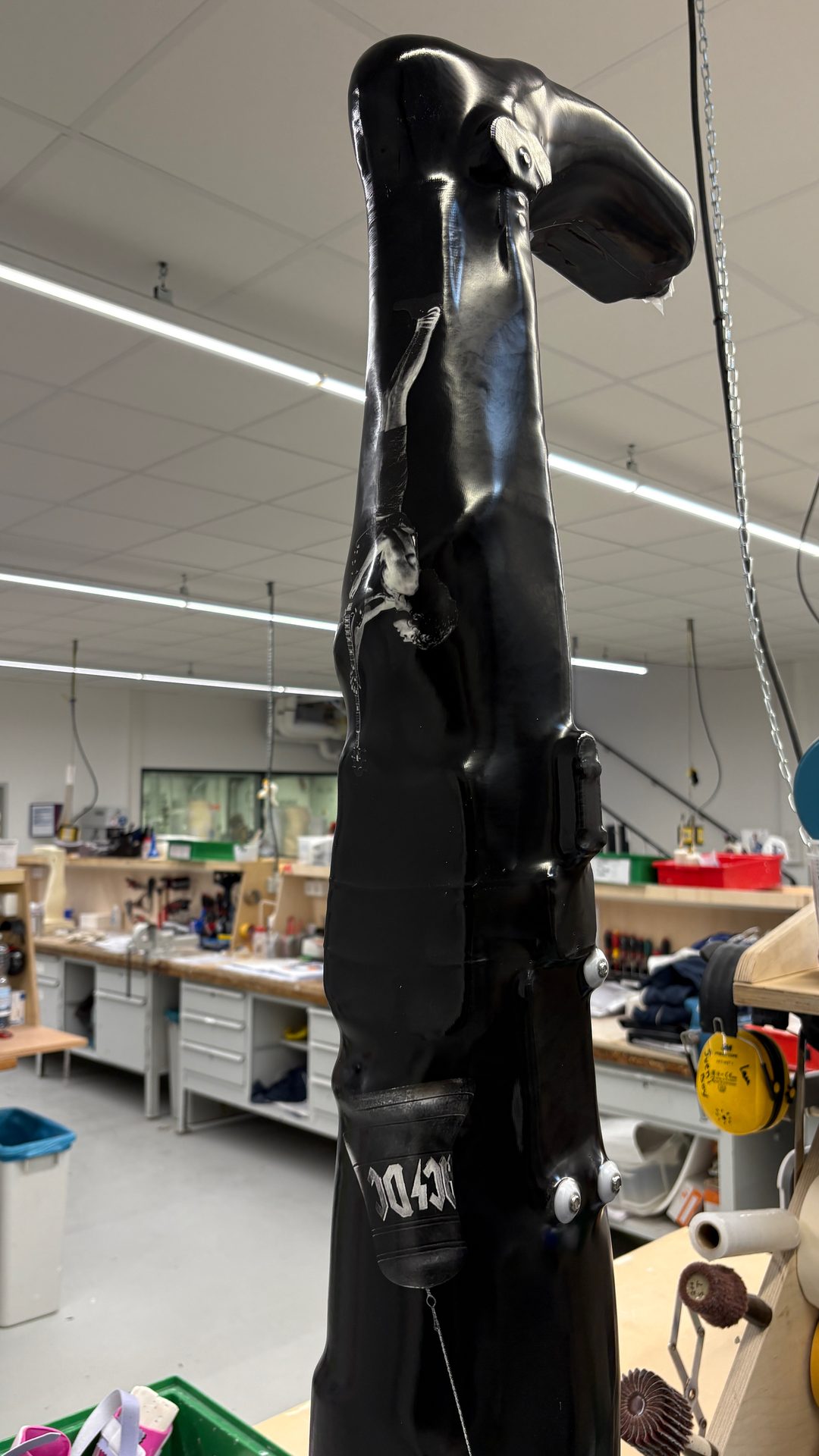 Black prosthetic or industrial device with an AC/DC logo and a figure print, in a workshop setting.