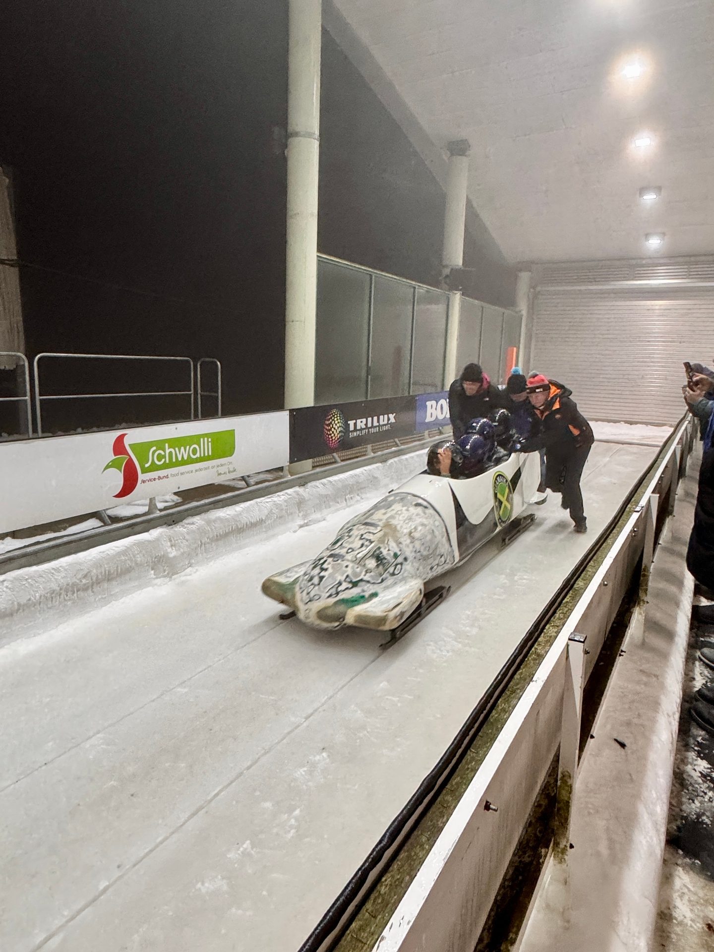Bobsled team pushing a bobsled on an icy track under artificial lights.