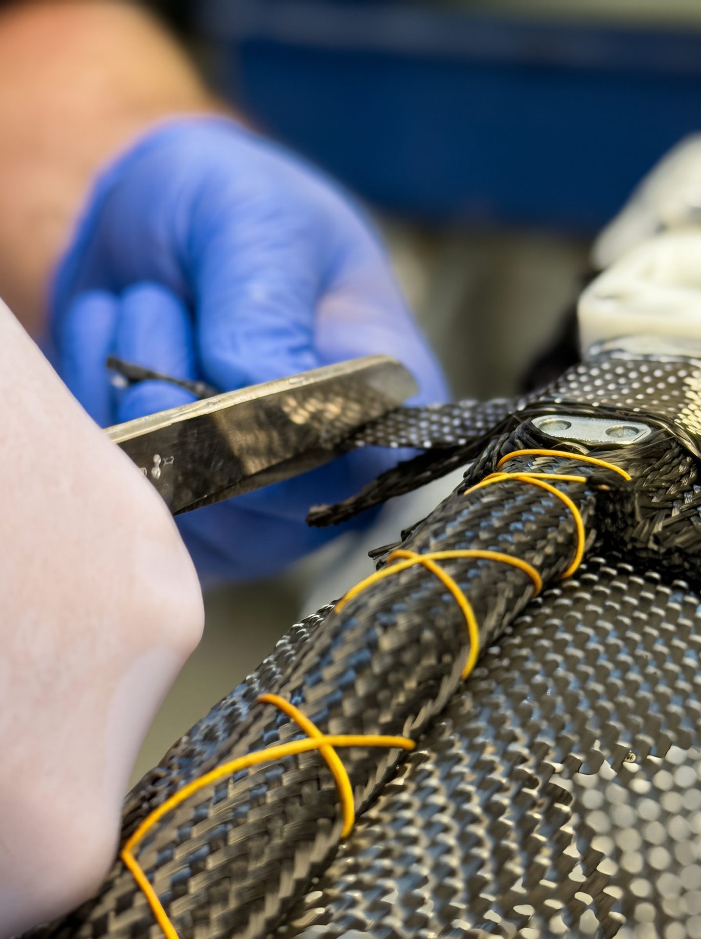 Person in blue glove manipulates braided carbon fiber with a tool, secured by yellow bands.