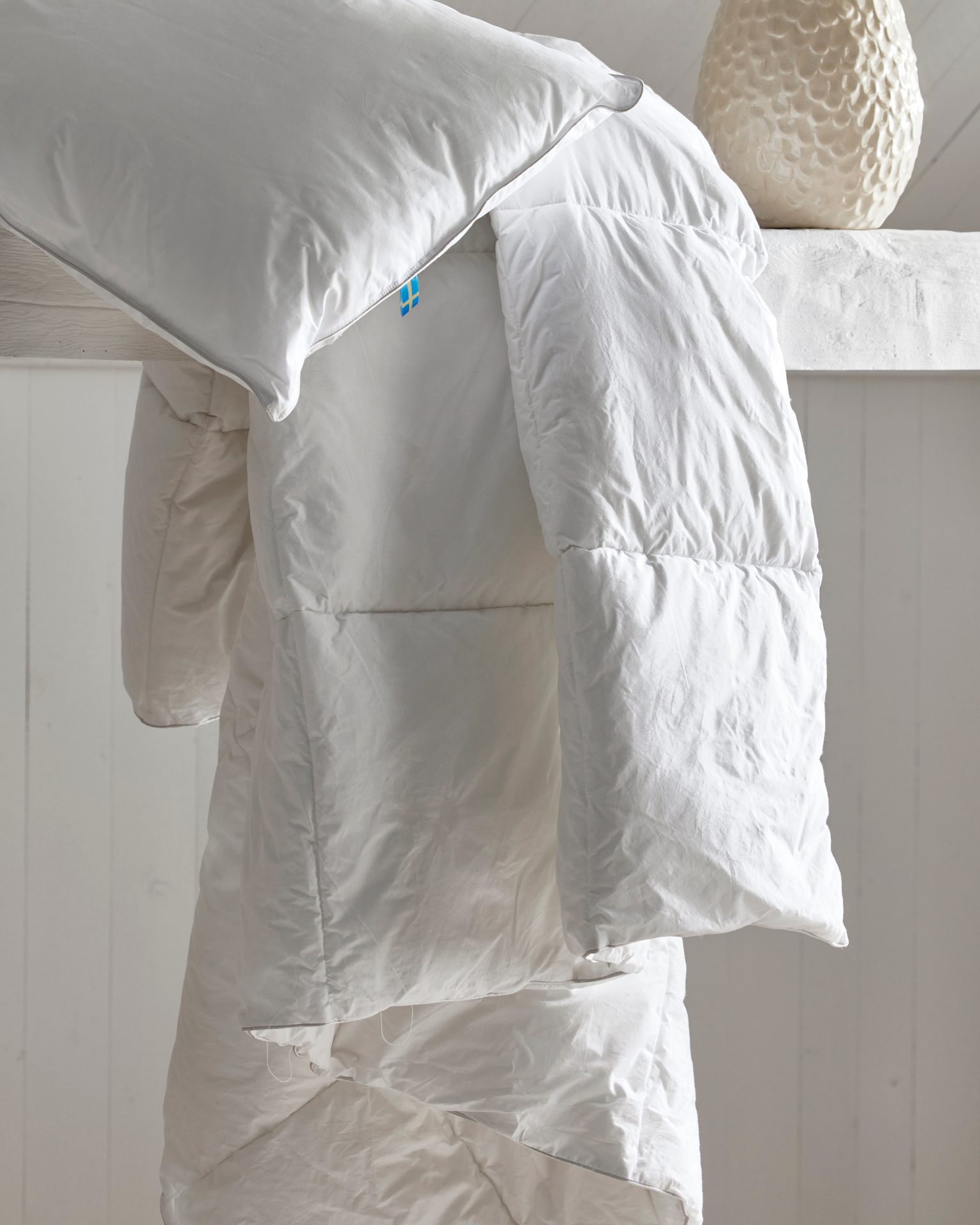 Soft white pillow and duvet draped over a shelf, emphasizing comfort and plush texture.