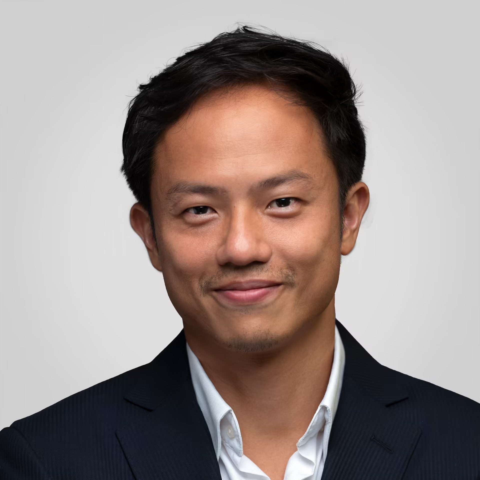 Headshot of a smiling East Asian man in a dark suit and white shirt.