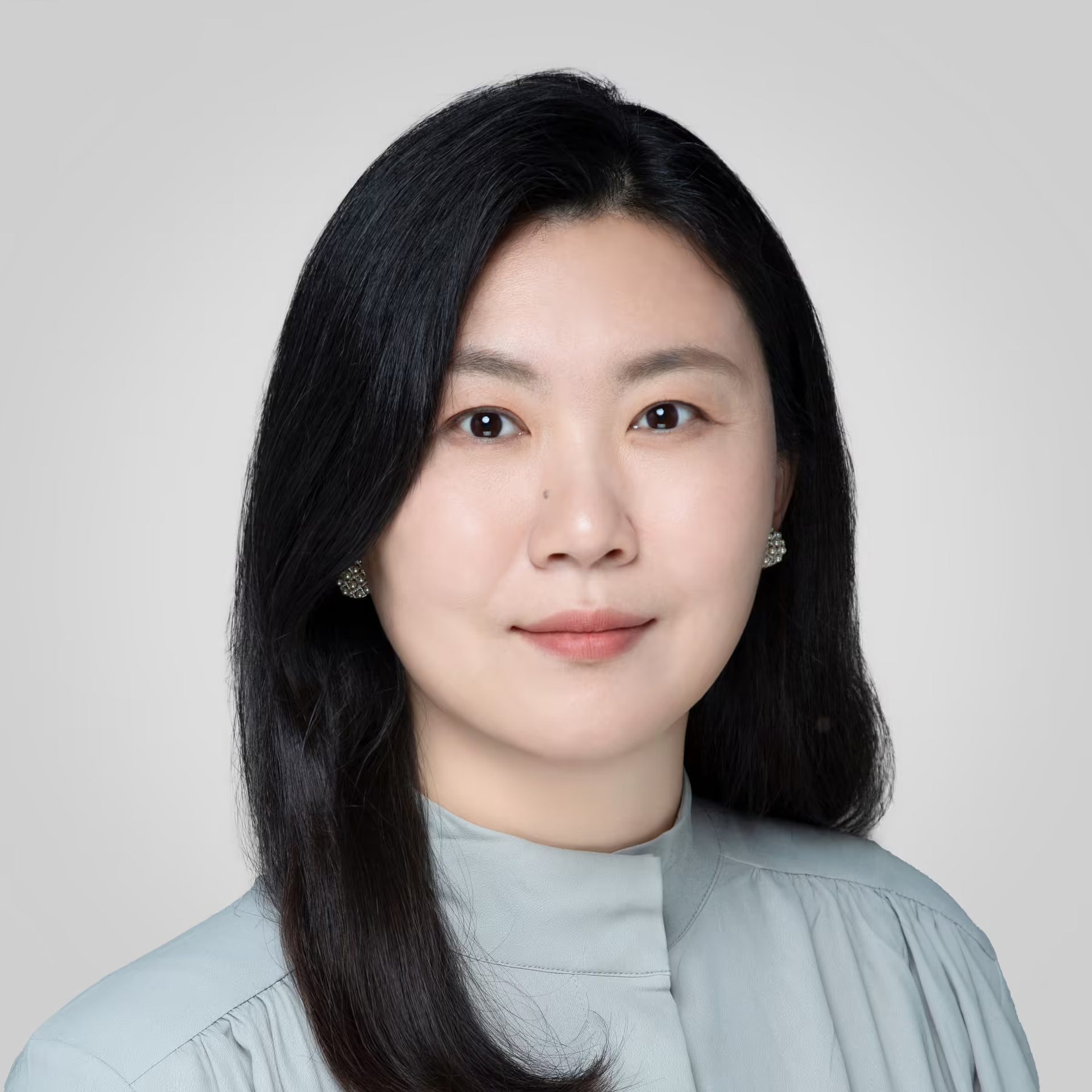 Portrait of an Asian woman with long dark hair, light blue top, and earrings, with a slight smile.
