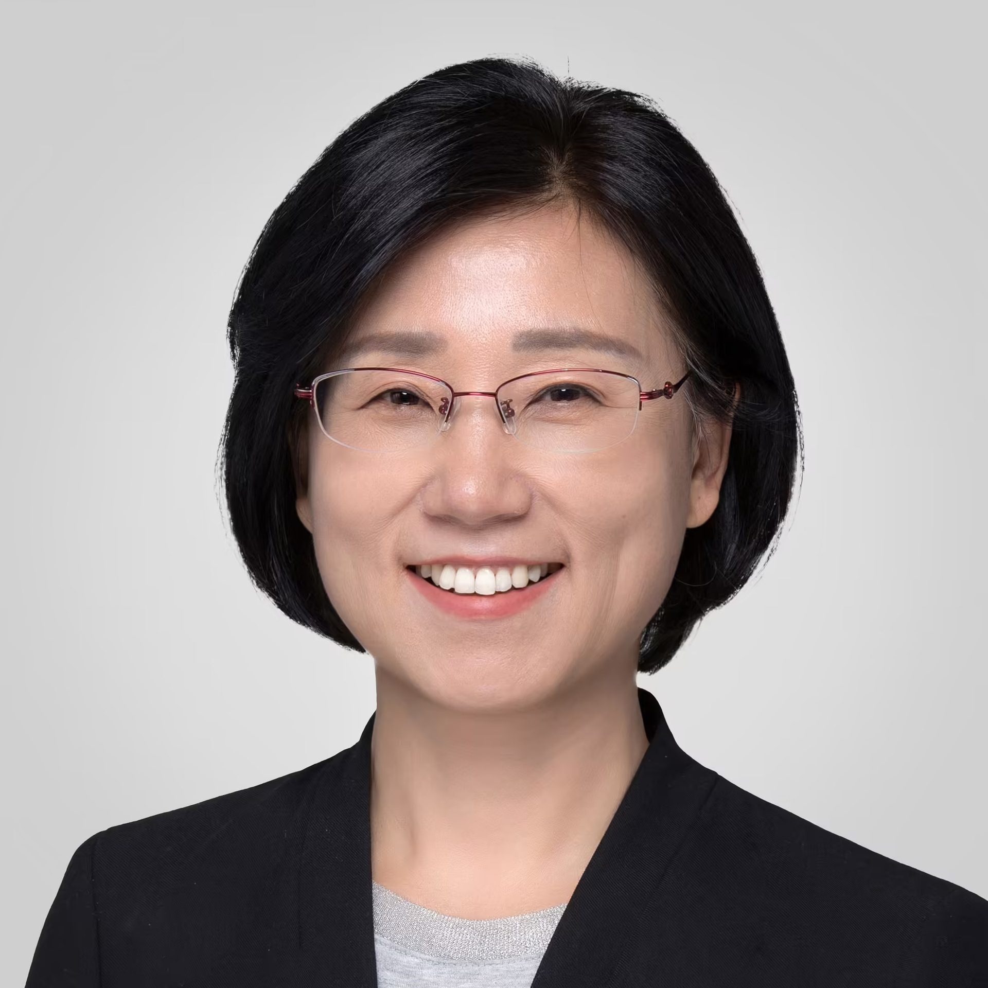 Smiling Asian woman with short dark hair, red glasses, and a black blazer.