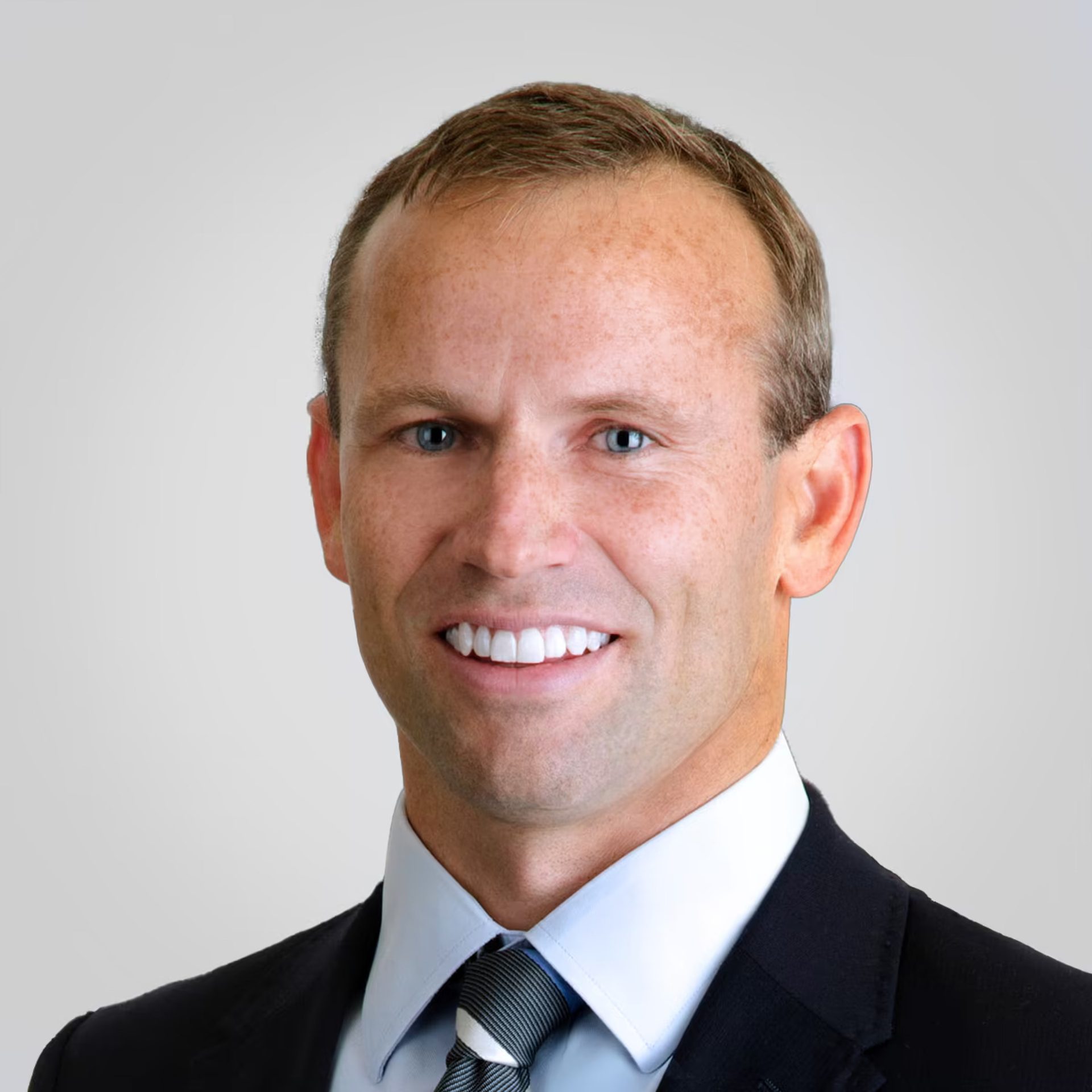Headshot of a smiling man in a suit and tie against a plain background.