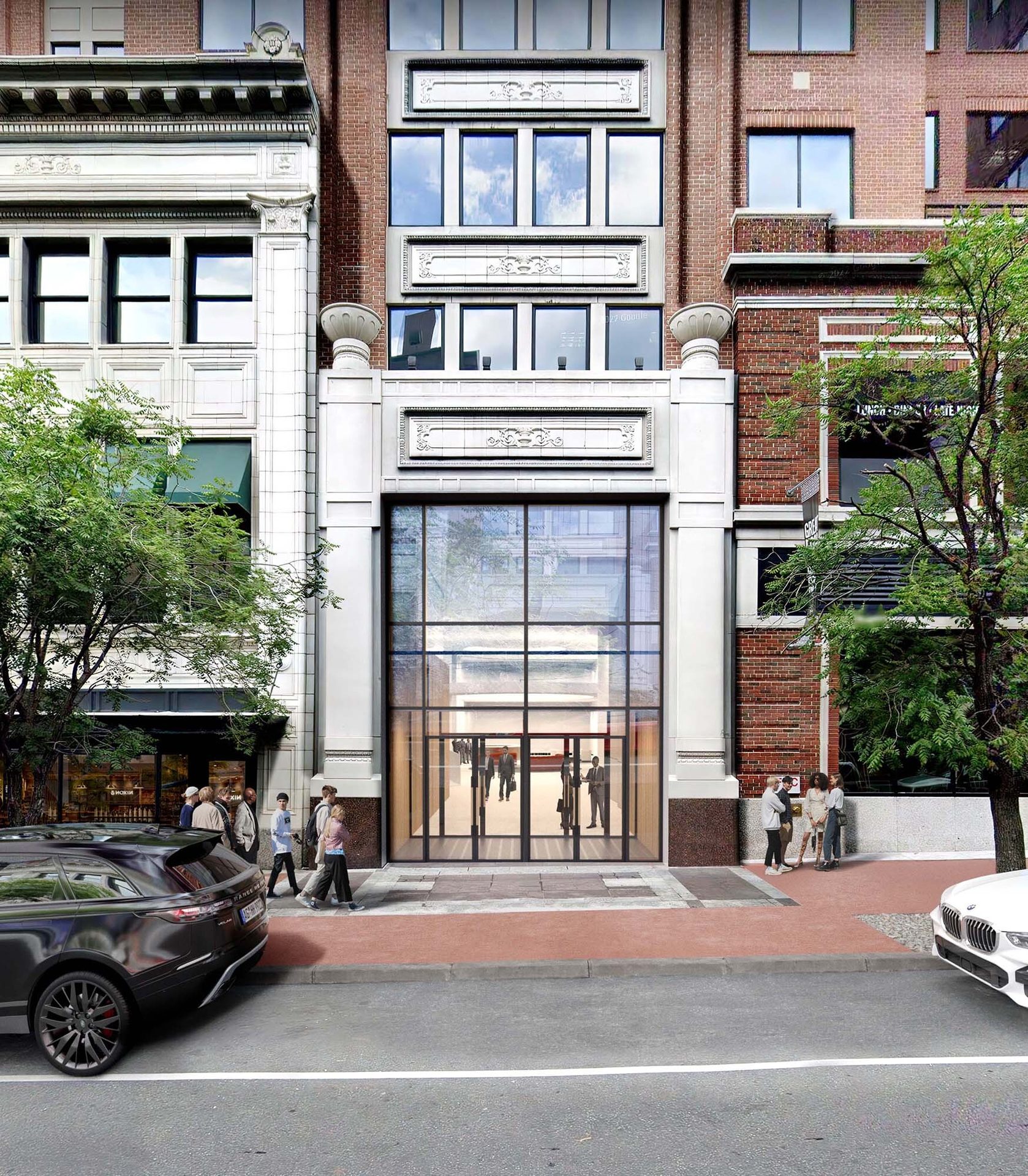 A large glass entrance in a multi-story building with a white facade and brick accents, people on sidewalk.