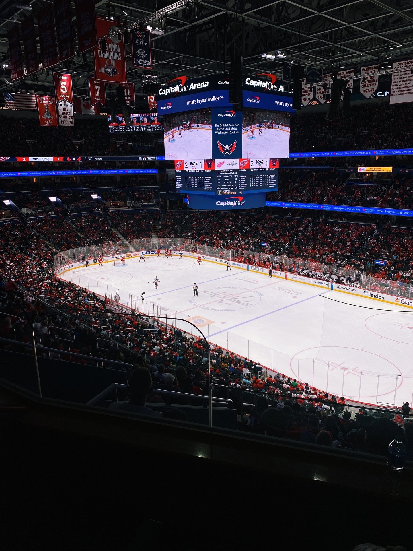 An ice hockey game in an arena, with players, fans, large screens, and championship banners overhead.