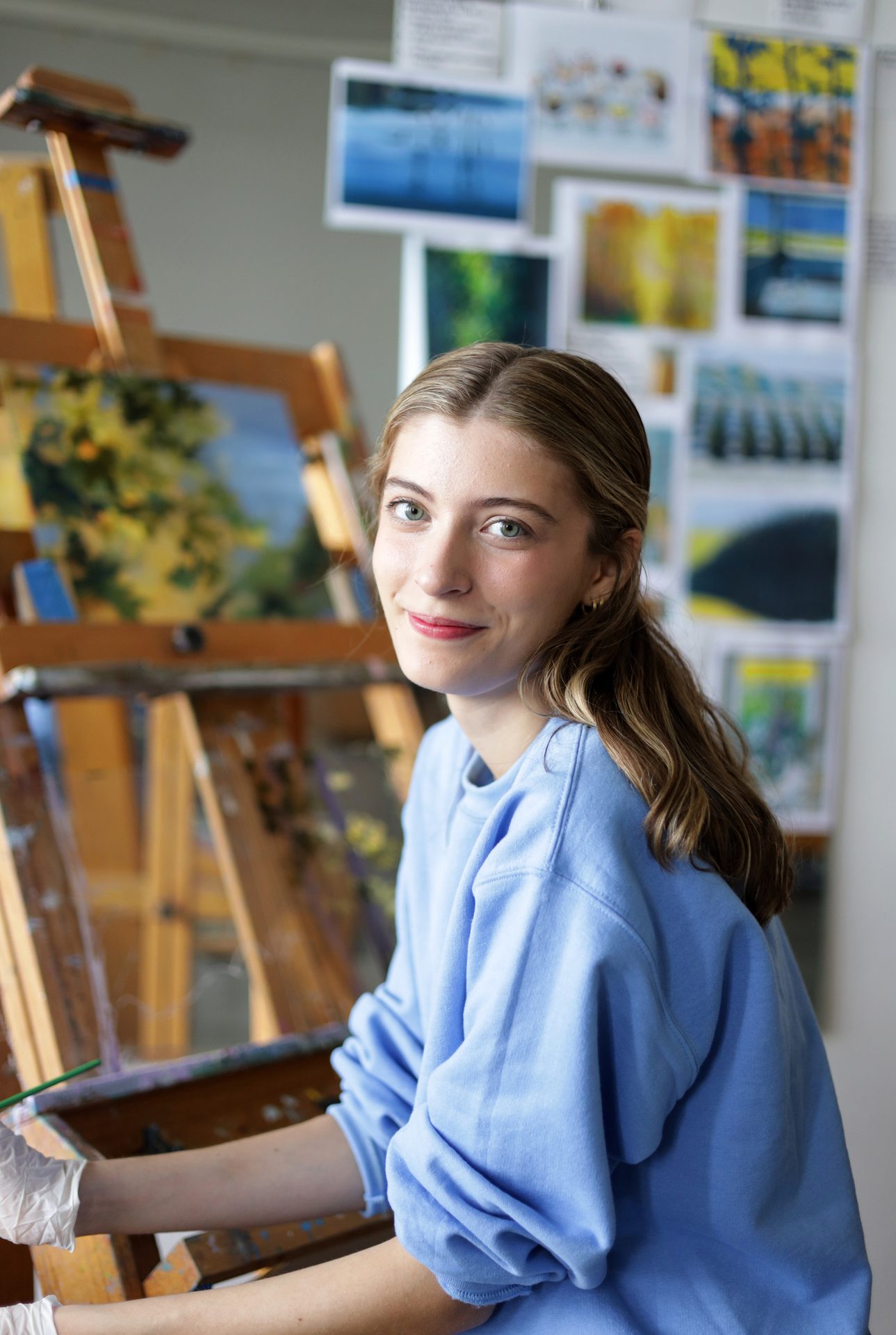 Young woman smiling while painting at an easel.