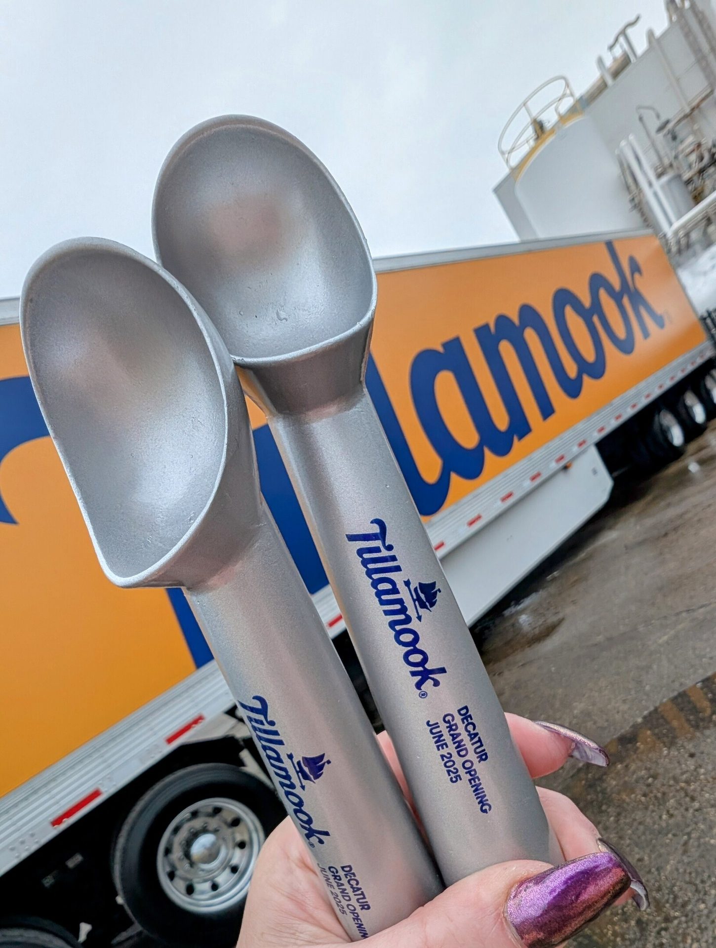 Two Tillamook scoops, labeled 'Decatur Grand Opening June 2025', held near a Tillamook truck.