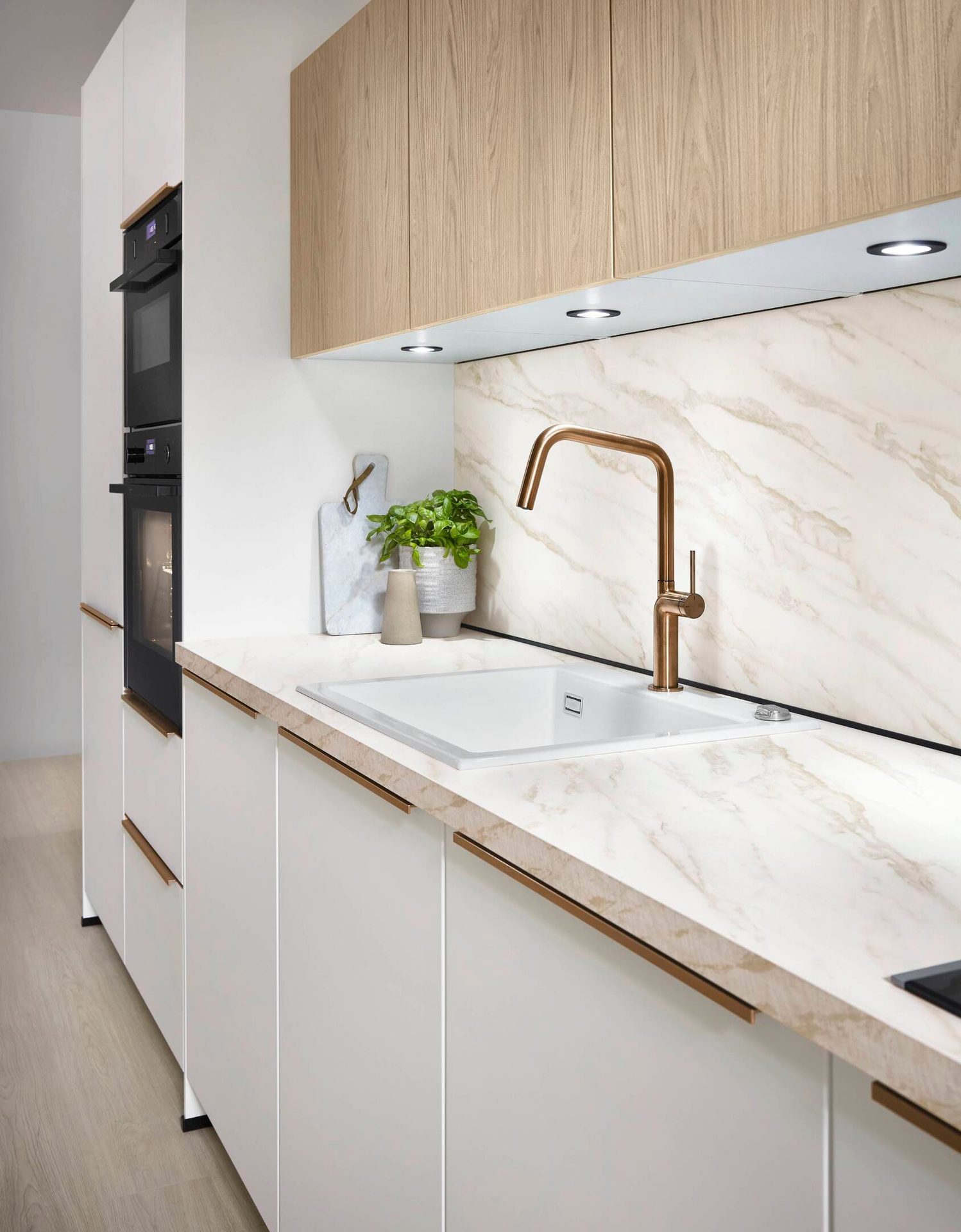 Modern white and wood kitchen with marble counters, brass faucet, and built-in appliances.