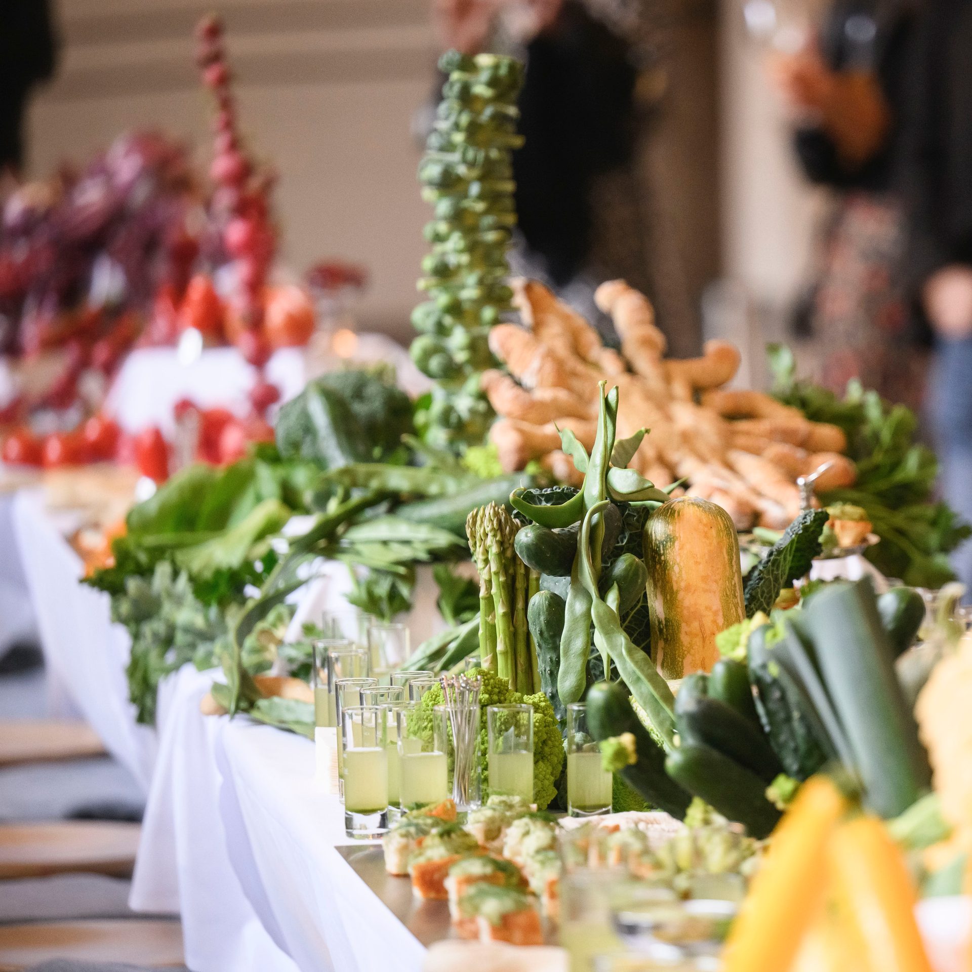 A vibrant buffet table laden with fresh green vegetables, appetizers, and green juice shots, catering to health-conscious diners.