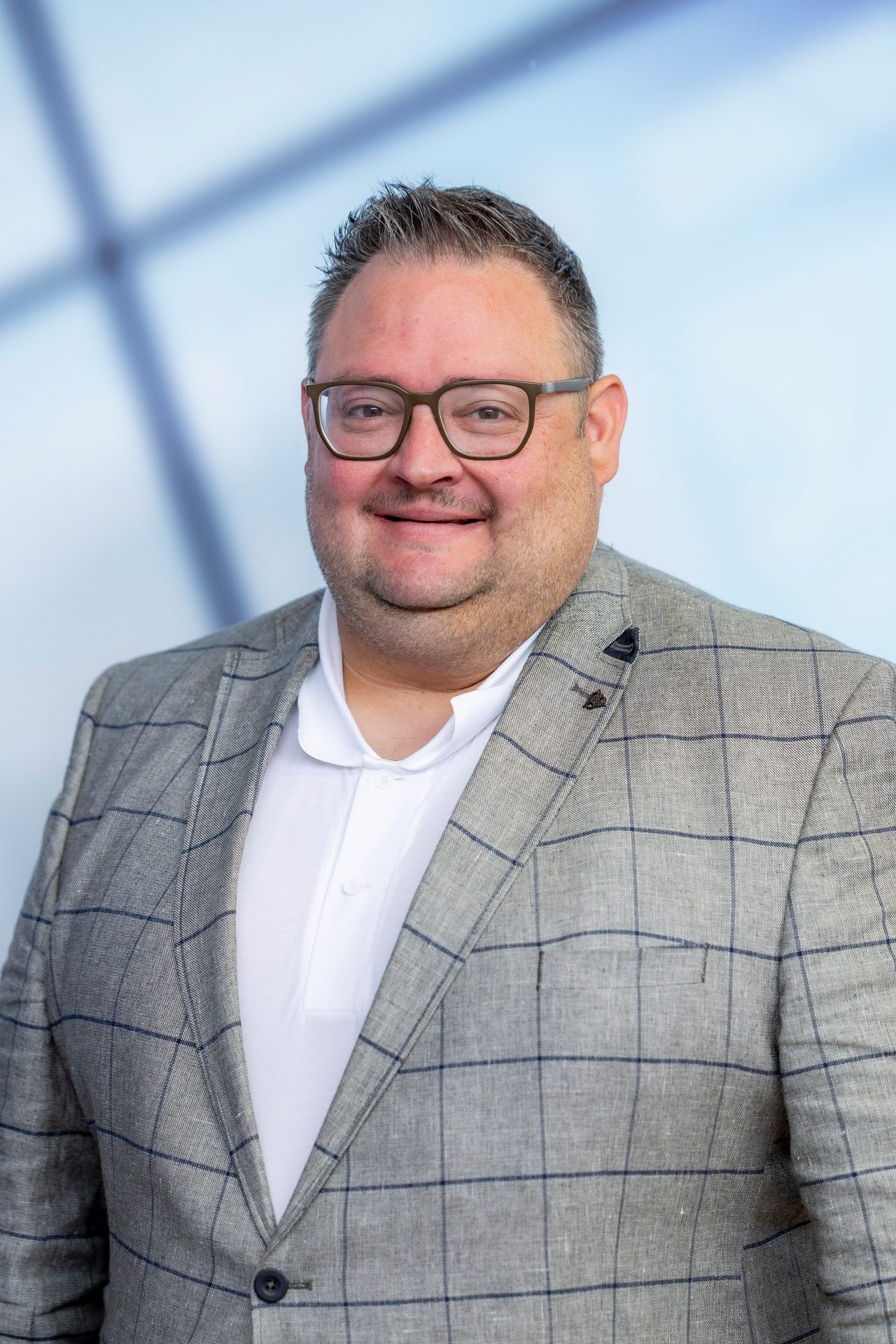 Smiling man in glasses and plaid blazer looking at the camera.
