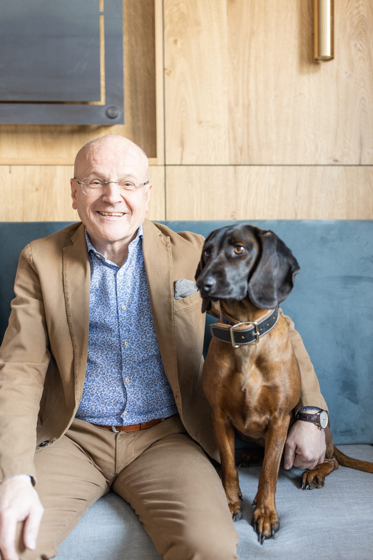 A smiling man and a brown dog sit side-by-side on a blue couch.