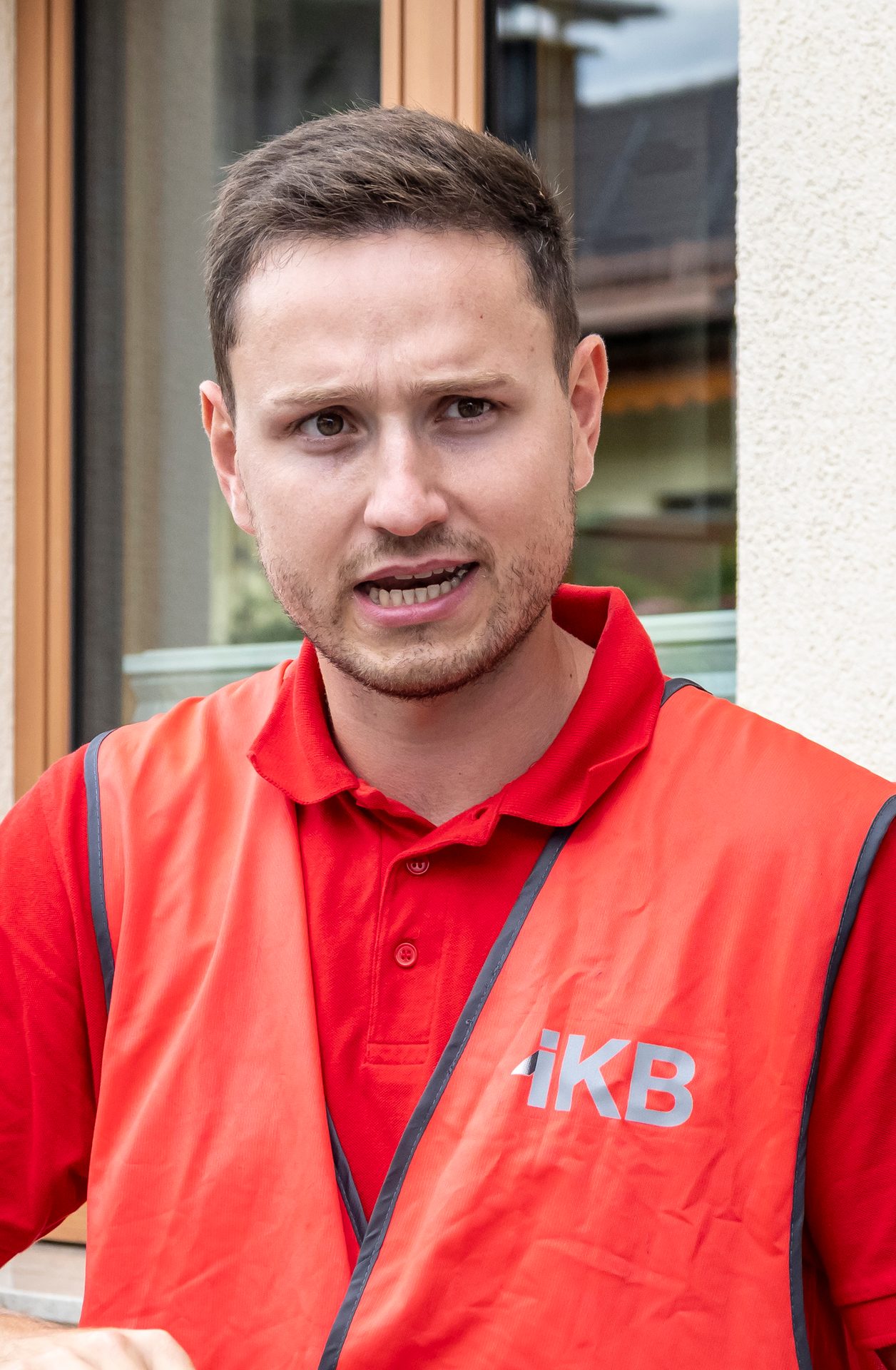 Man in red polo and orange "iKB" vest, speaking.