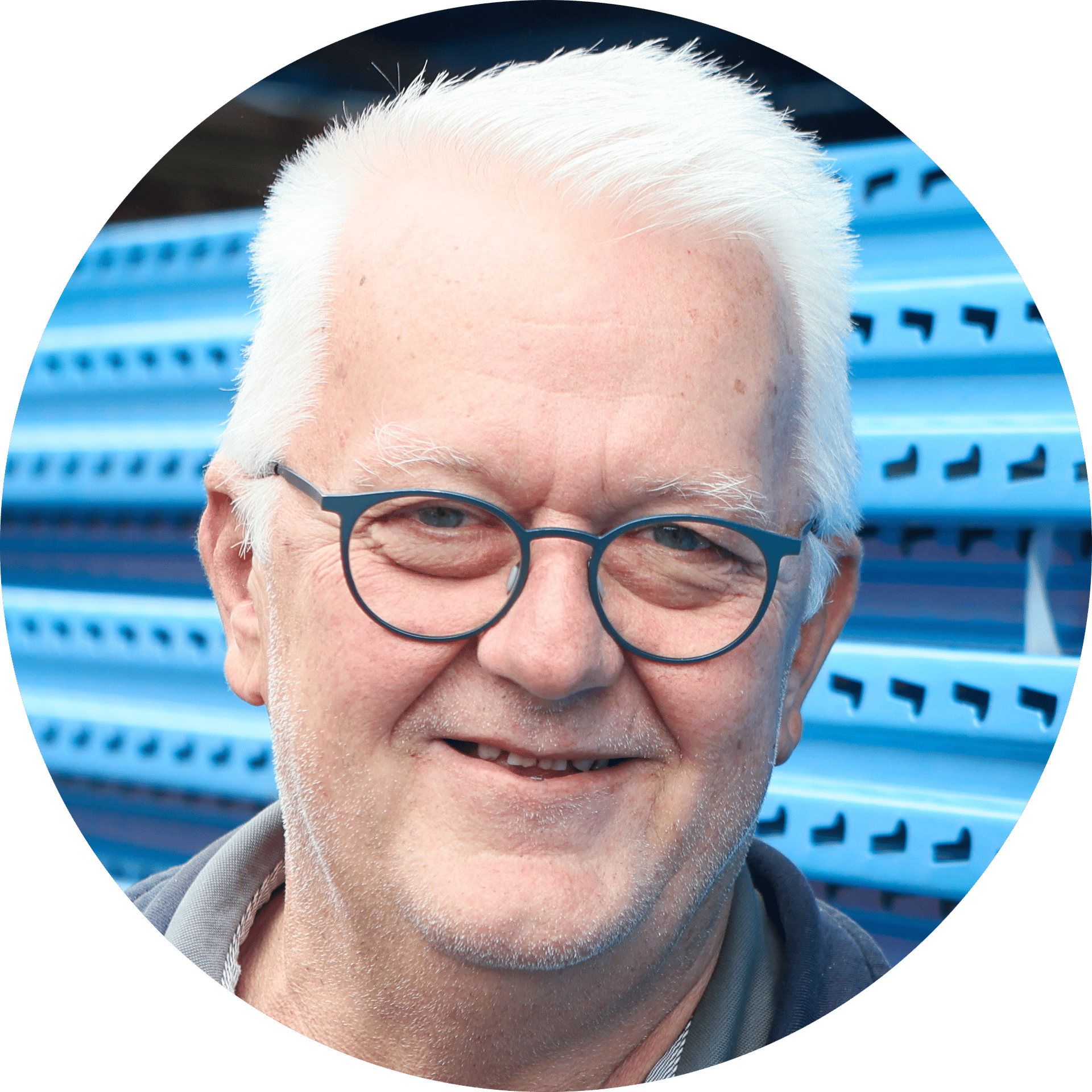 Close-up portrait of a smiling older man with white hair and glasses, against a blue background.