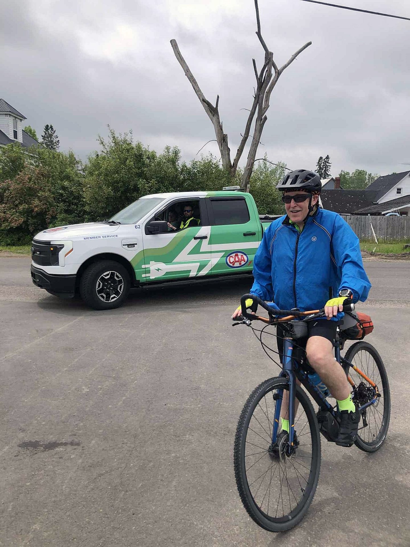 Man in blue jacket on bicycle next to a white and green CAA electric truck.