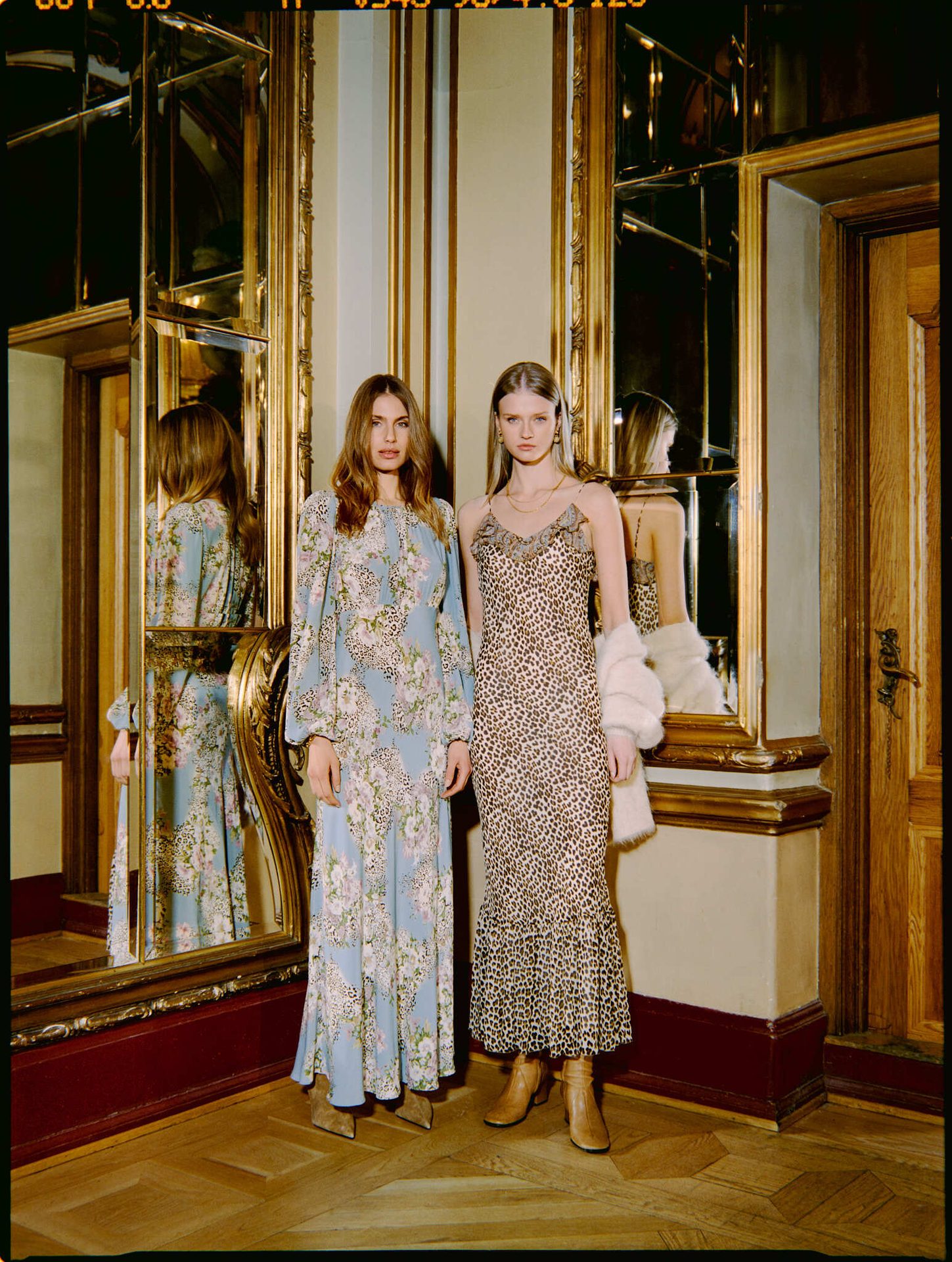 Two women in elegant dresses, one blue floral and leopard, one leopard slip, in an ornate room.