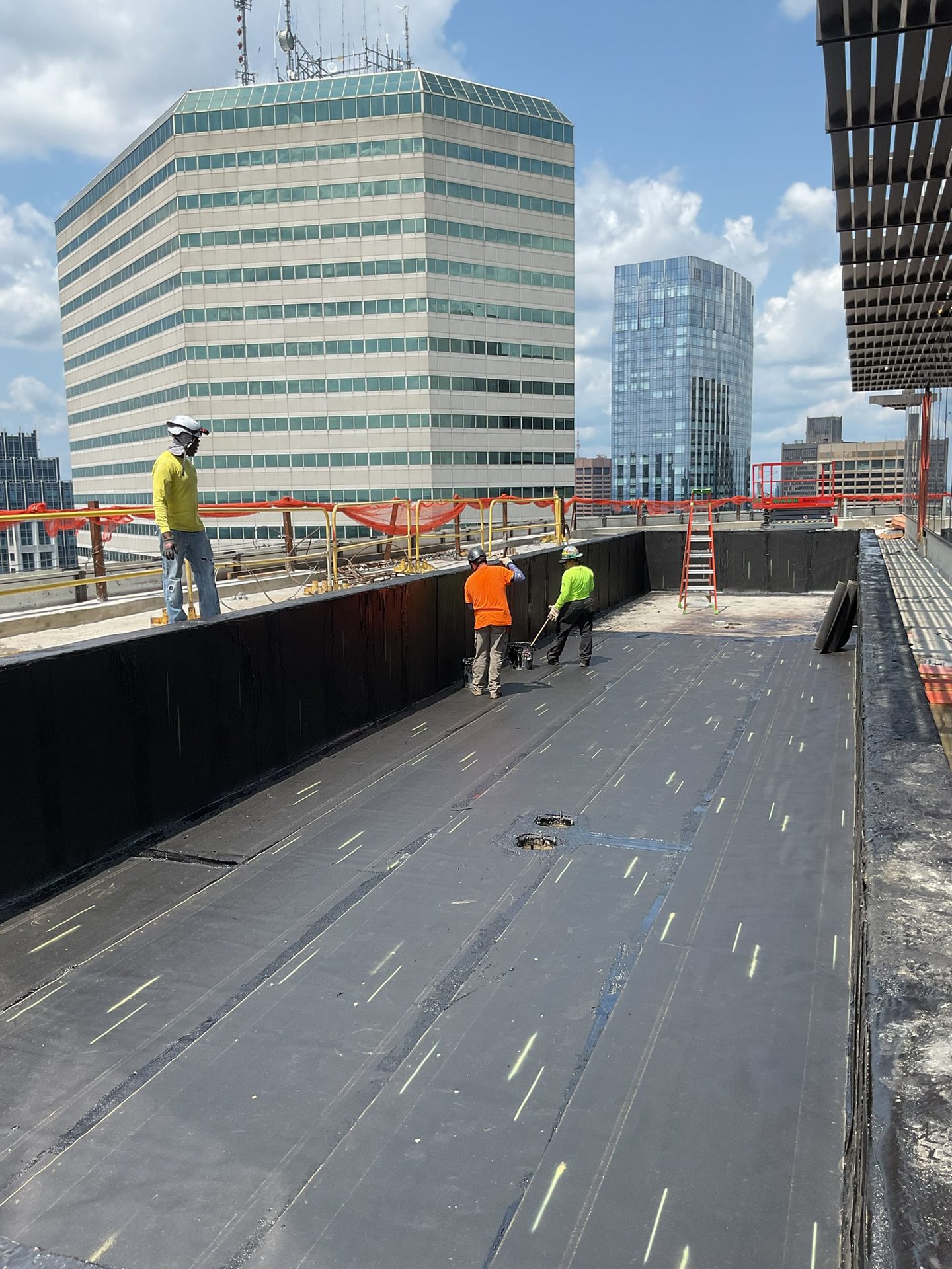 Workers preparing a flat rooftop, with a large hexagonal building and other city structures in the background.