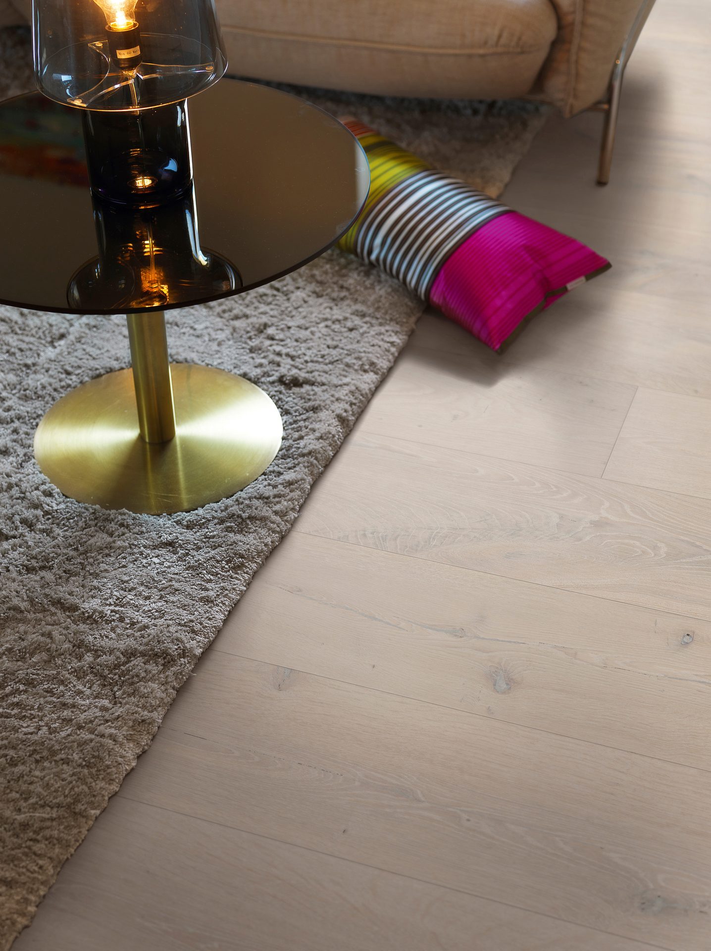 Close-up of a modern lamp on a glass table, with a fluffy rug, bright cushion, and light wood floor.