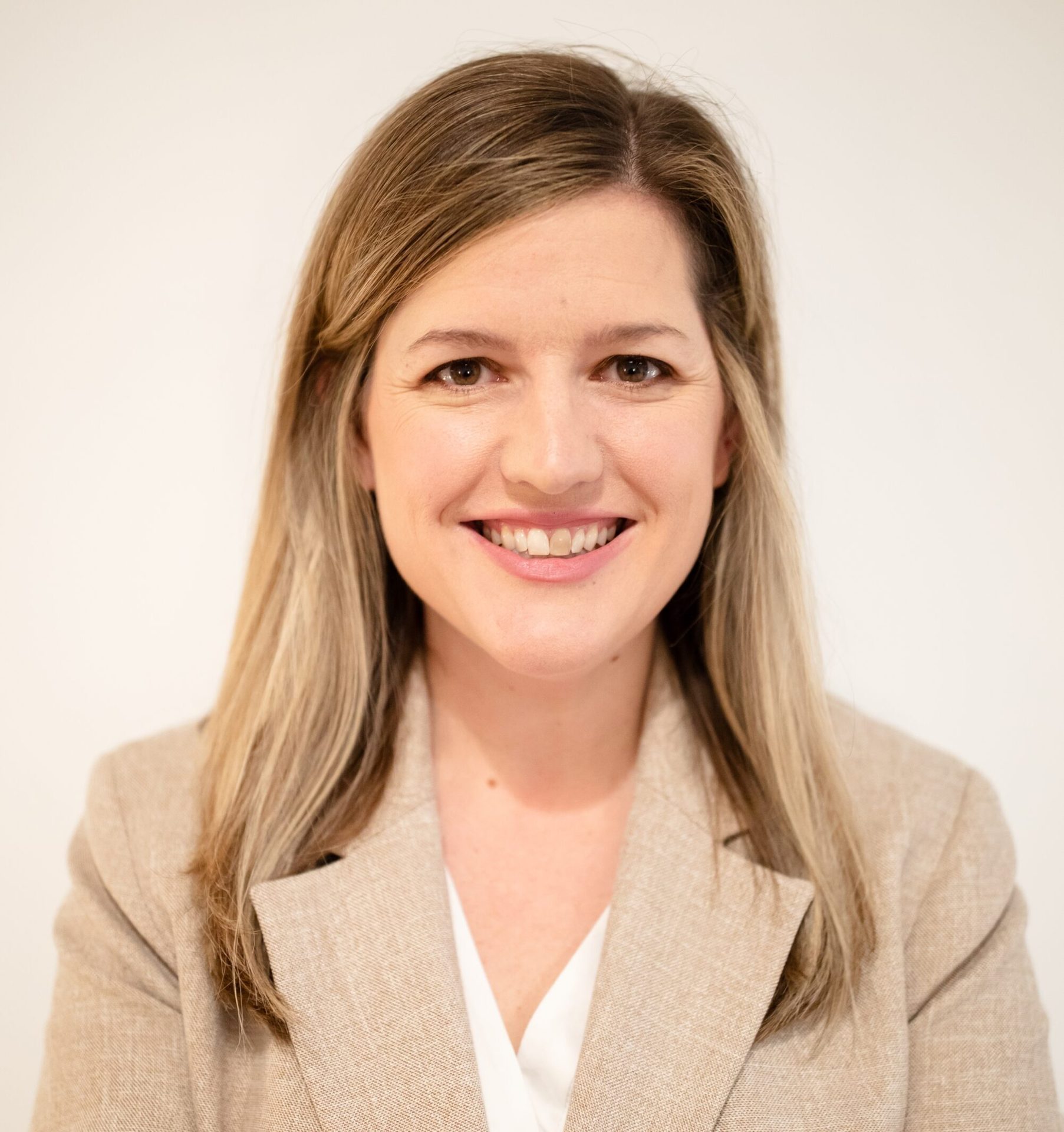 Smiling woman with long blonde hair, wearing a beige blazer, looking directly at the viewer.