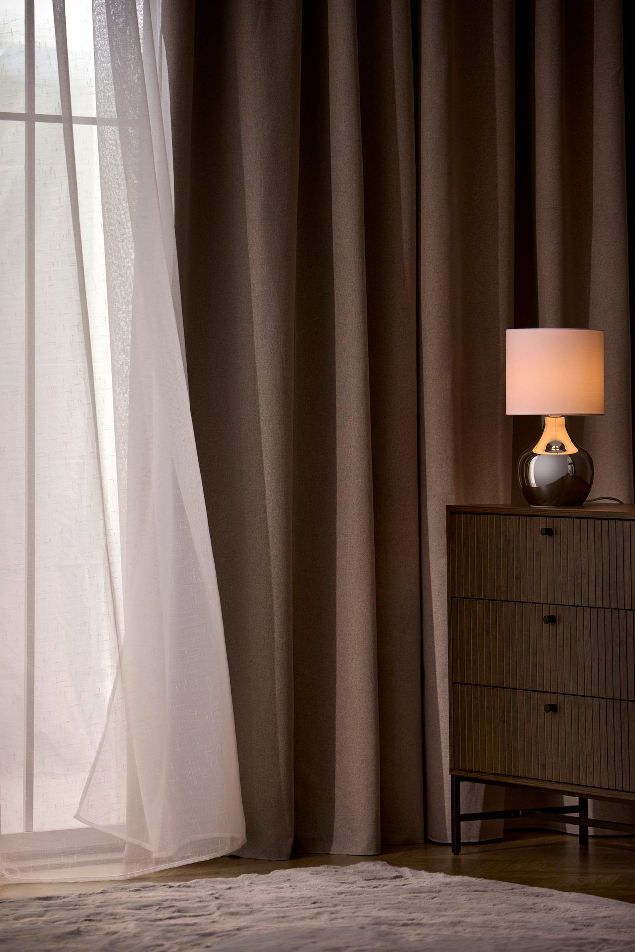 Window with curtains, lit lamp on dresser, and rug.