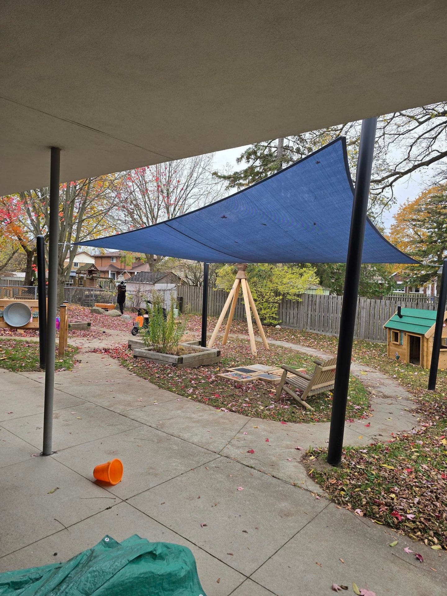 Outdoor play space at a child care centre with lots of natural elements, including a small garden, wooden structures and a tarp to provide shelter from weather. 