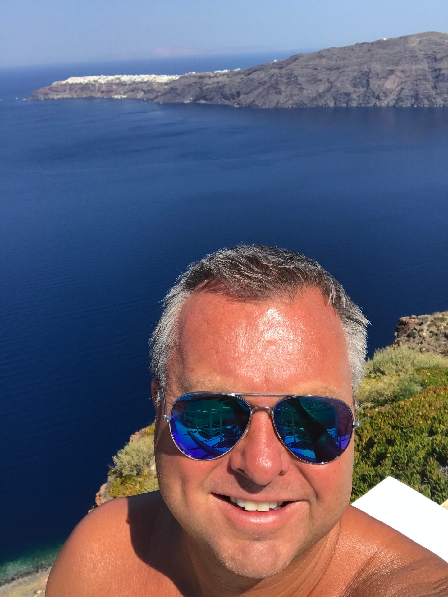 Smiling man in sunglasses with a blue sea and Santorini island in the background.
