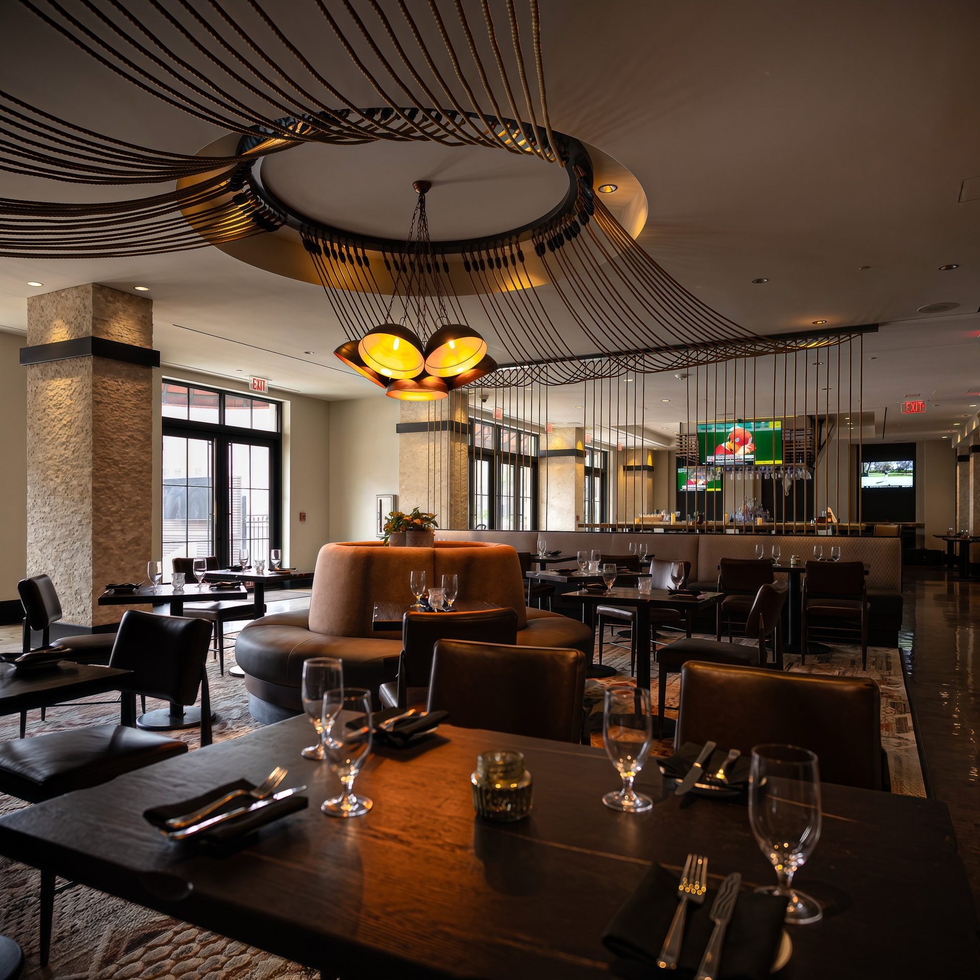Restaurant interior with dark tables, brown seating, and a unique rope and chandelier ceiling.