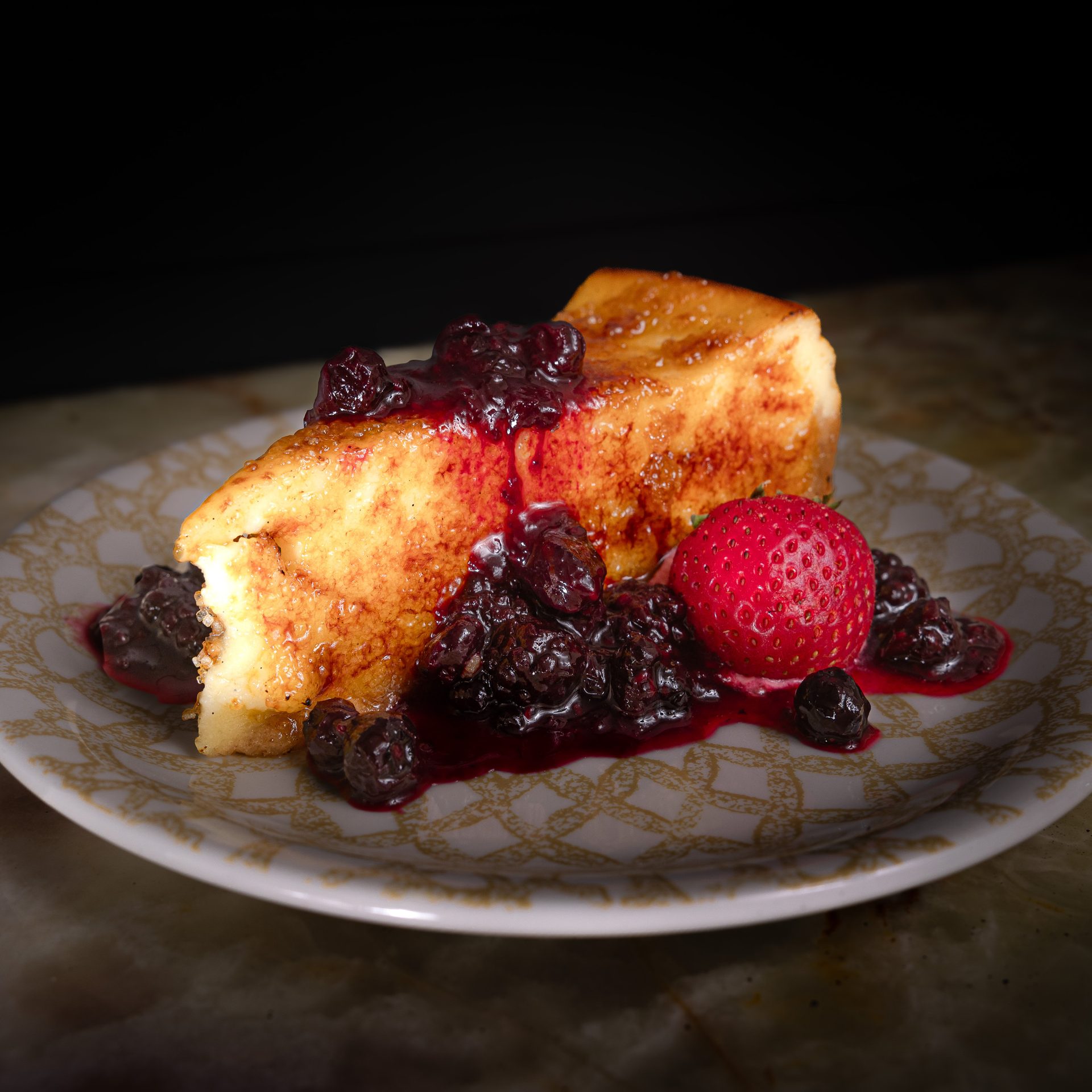 A slice of cheesecake topped with berries and a strawberry on a patterned plate.