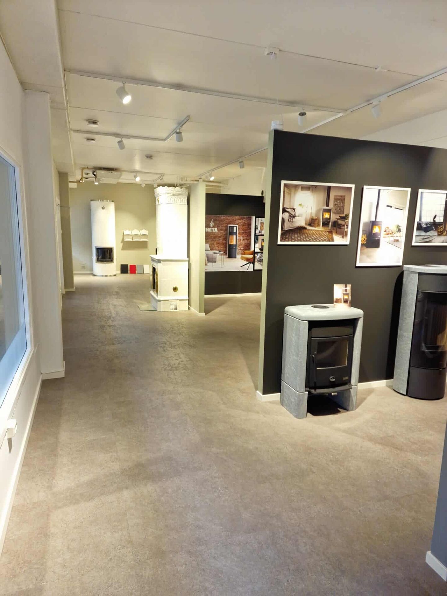 Showroom displaying various modern and traditional wood-burning stoves and furnaces, with photos on walls.