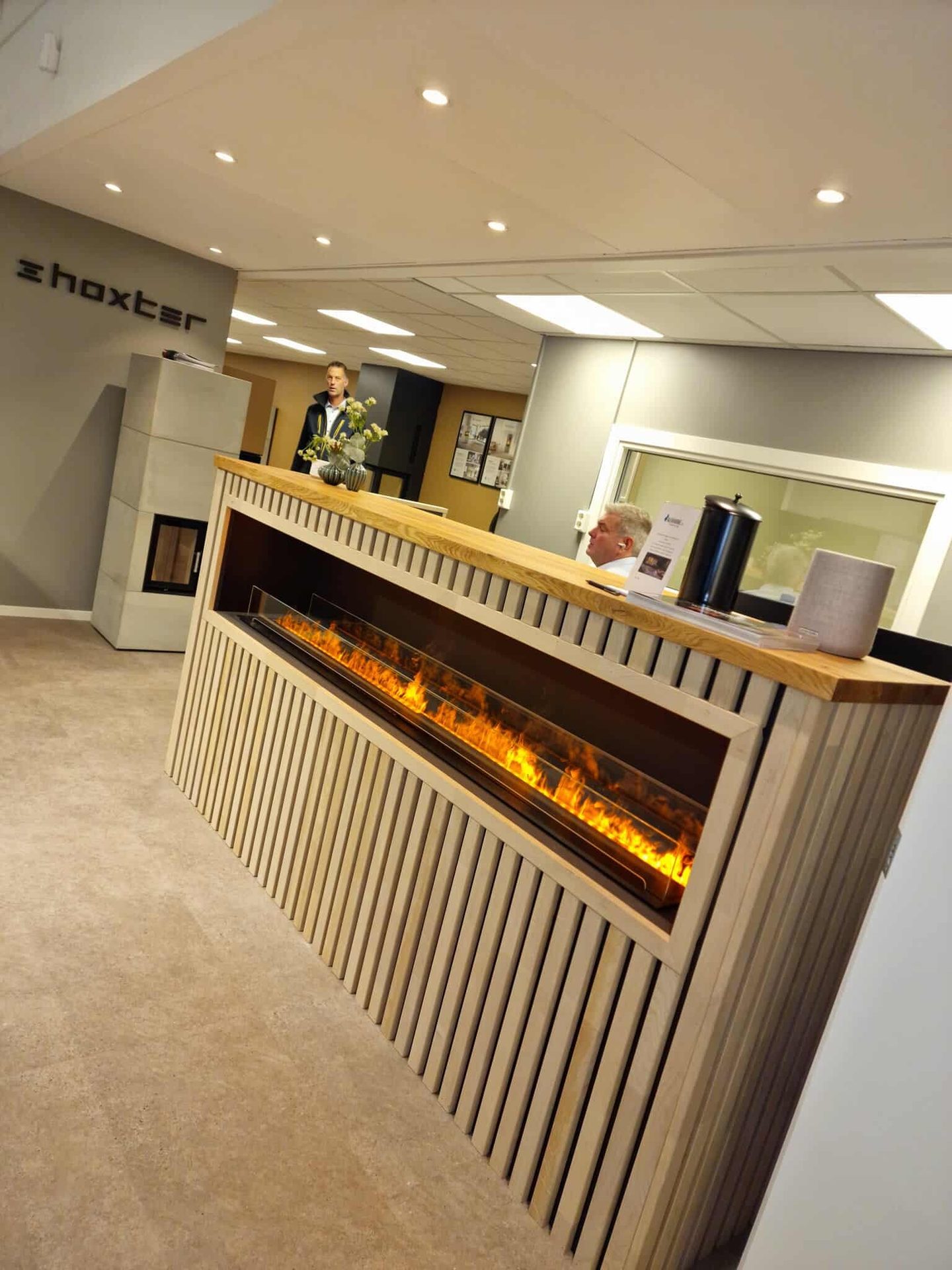 Modern reception desk with integrated long fireplace, 'Shoxter' logo, and two men in a showroom.