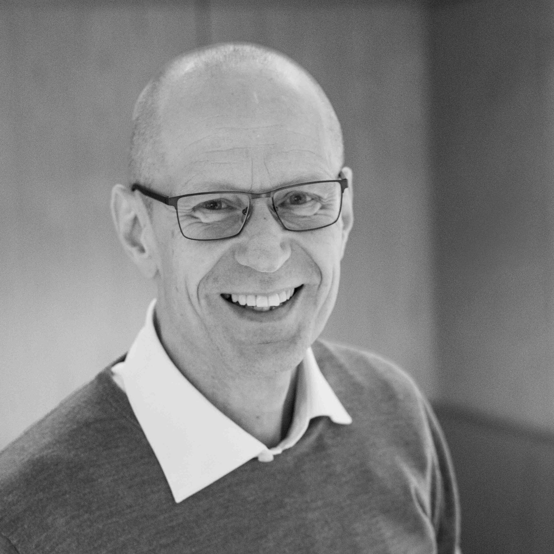 Black and white portrait of a bald man with glasses, smiling broadly at the camera.