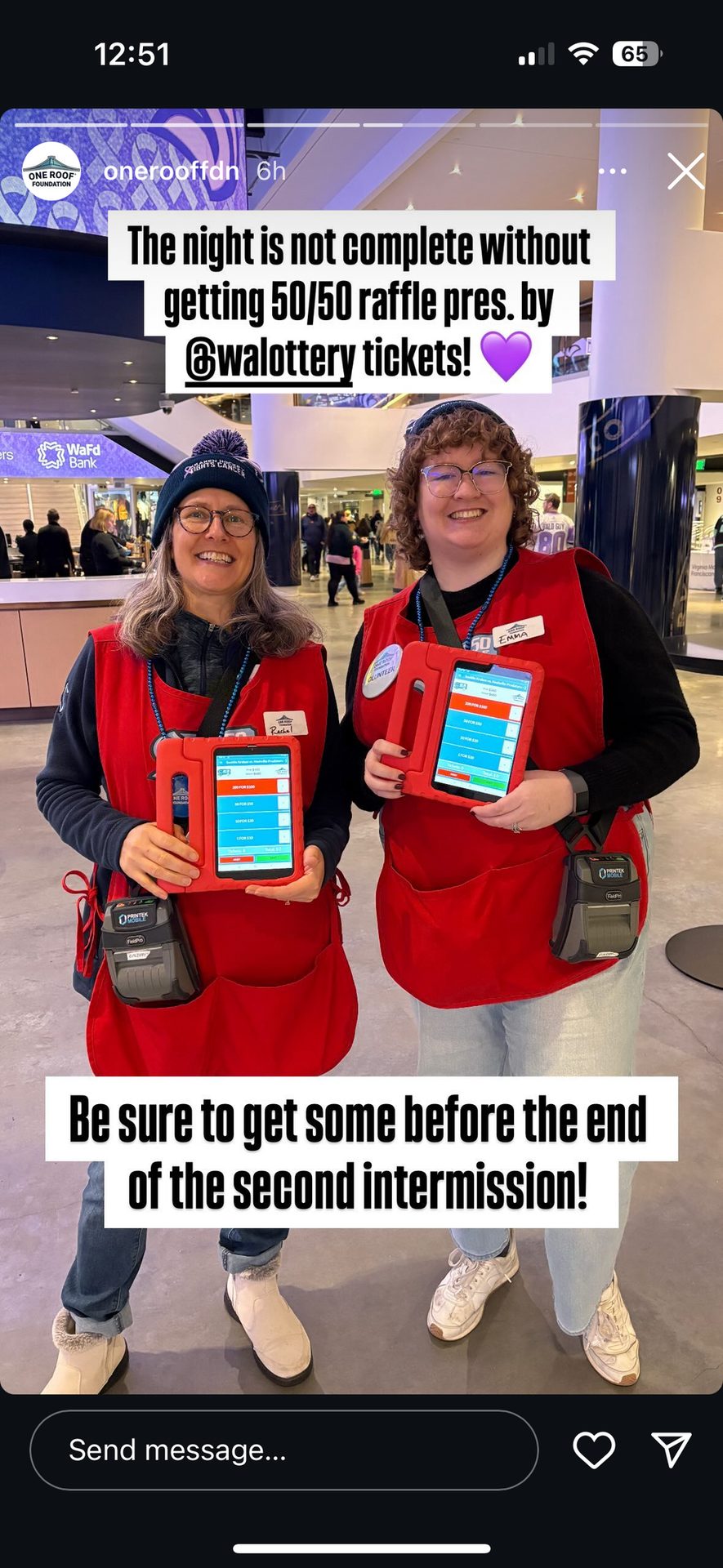 Two volunteers in red aprons hold tablets, selling lottery raffle tickets.