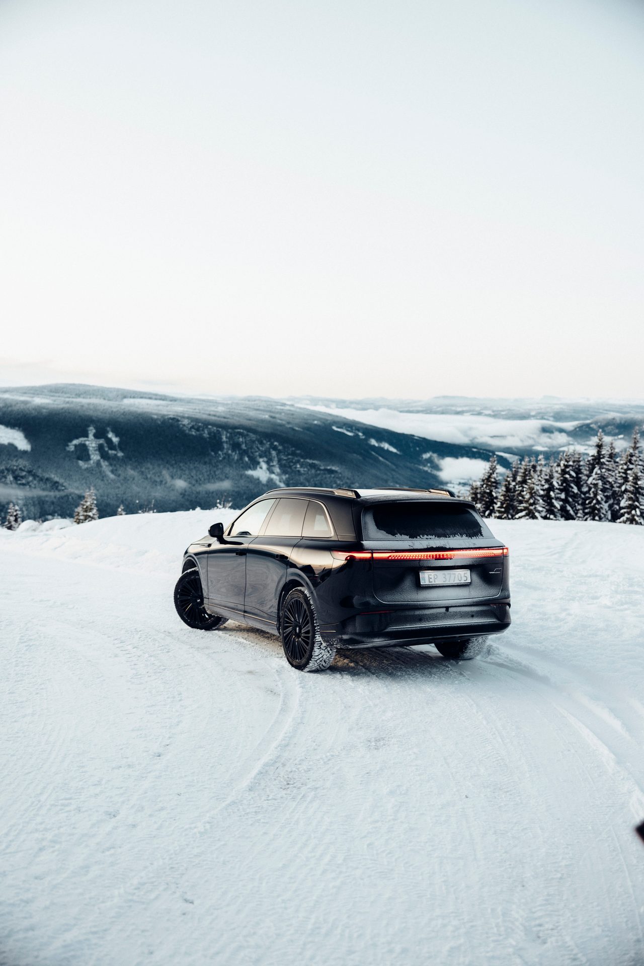 Black SUV parked on a snowy mountain road with a vast winter landscape and forest in the background.