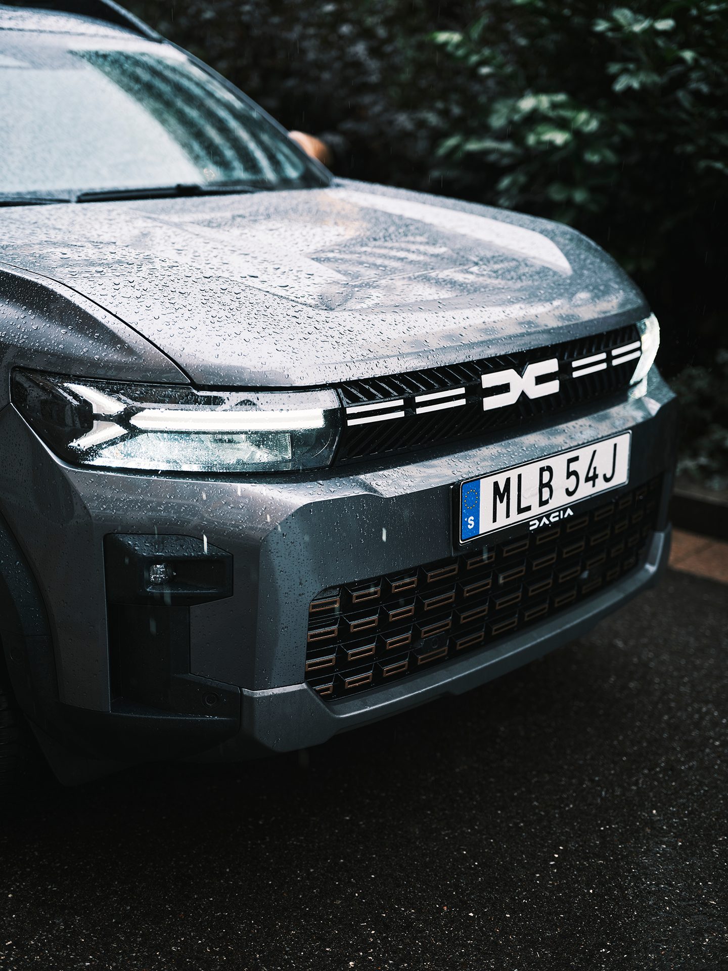 Close-up of a grey Dacia car front covered in raindrops, featuring its unique headlights and grille.