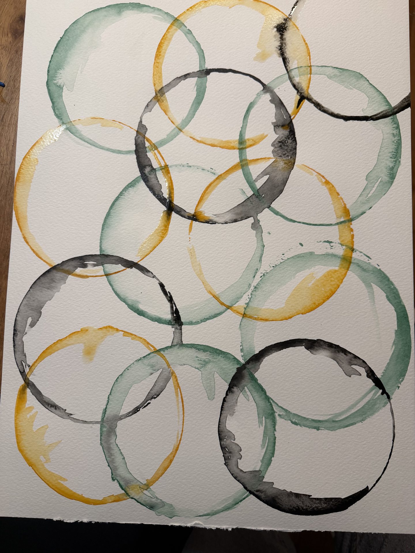 Watercolor painting of overlapping green, yellow, and black circles on a white background.