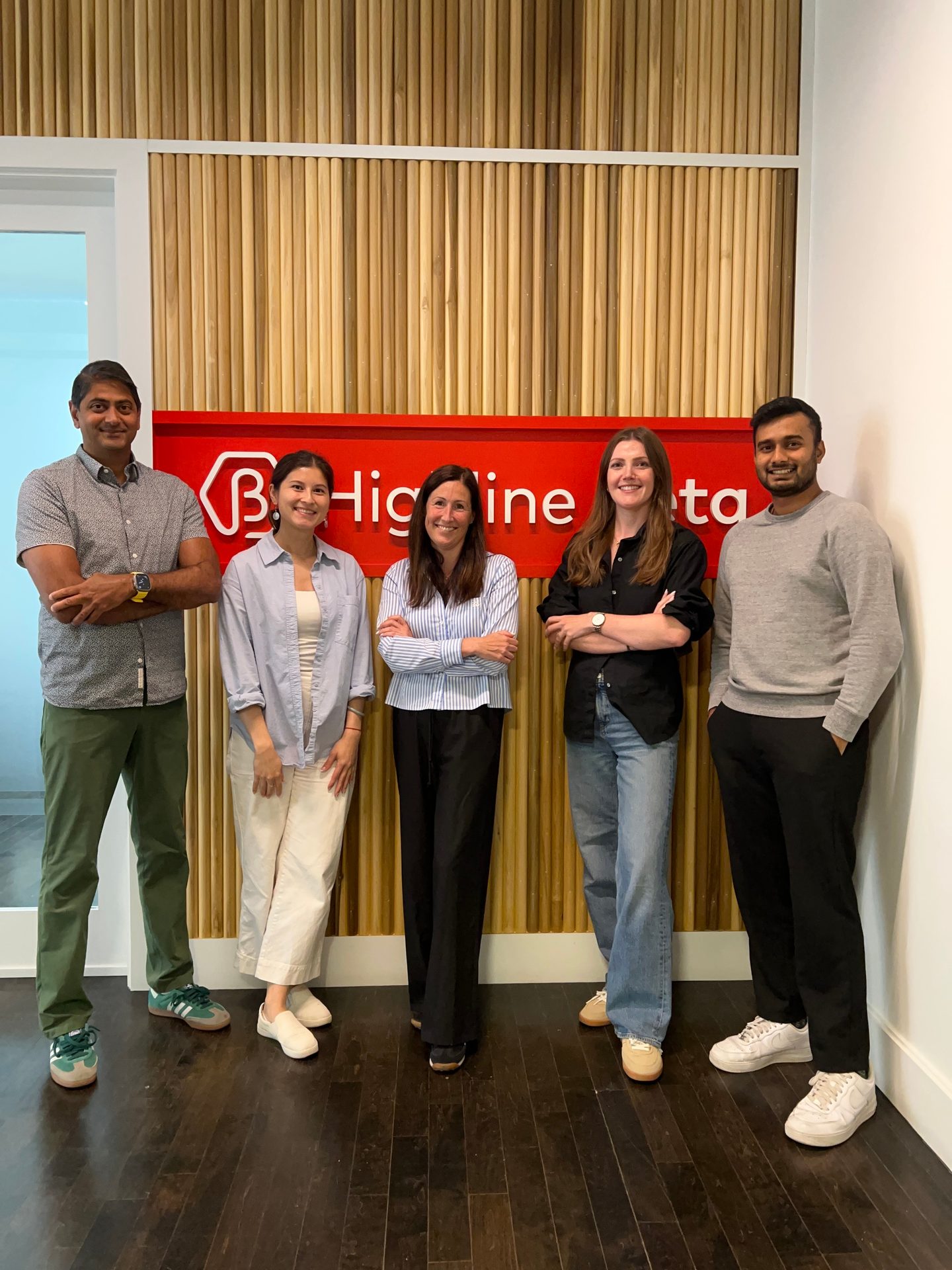Five people stand smiling in front of a red "Highline Data" sign on a wooden slatted wall.