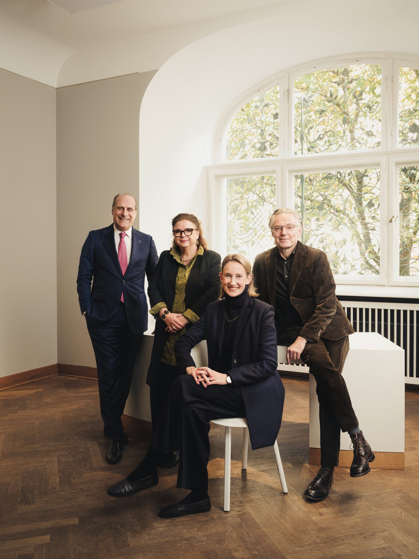 Four people, two men and two women, posing indoors in front of a large arched window.