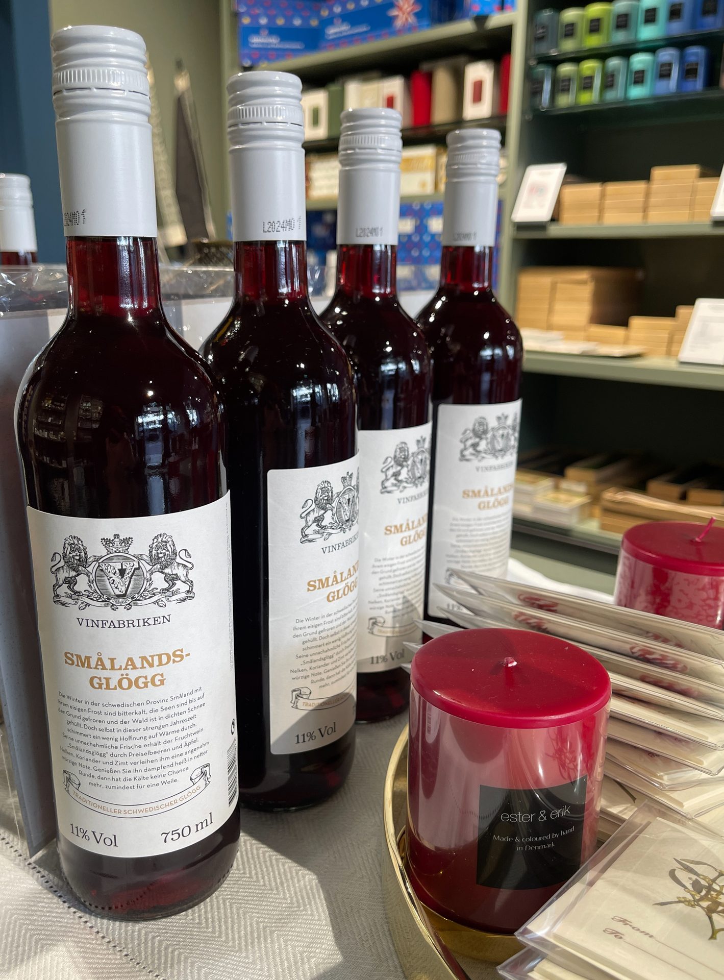 Several bottles of red Smålandsglögg and red ester & erik candles on a table.