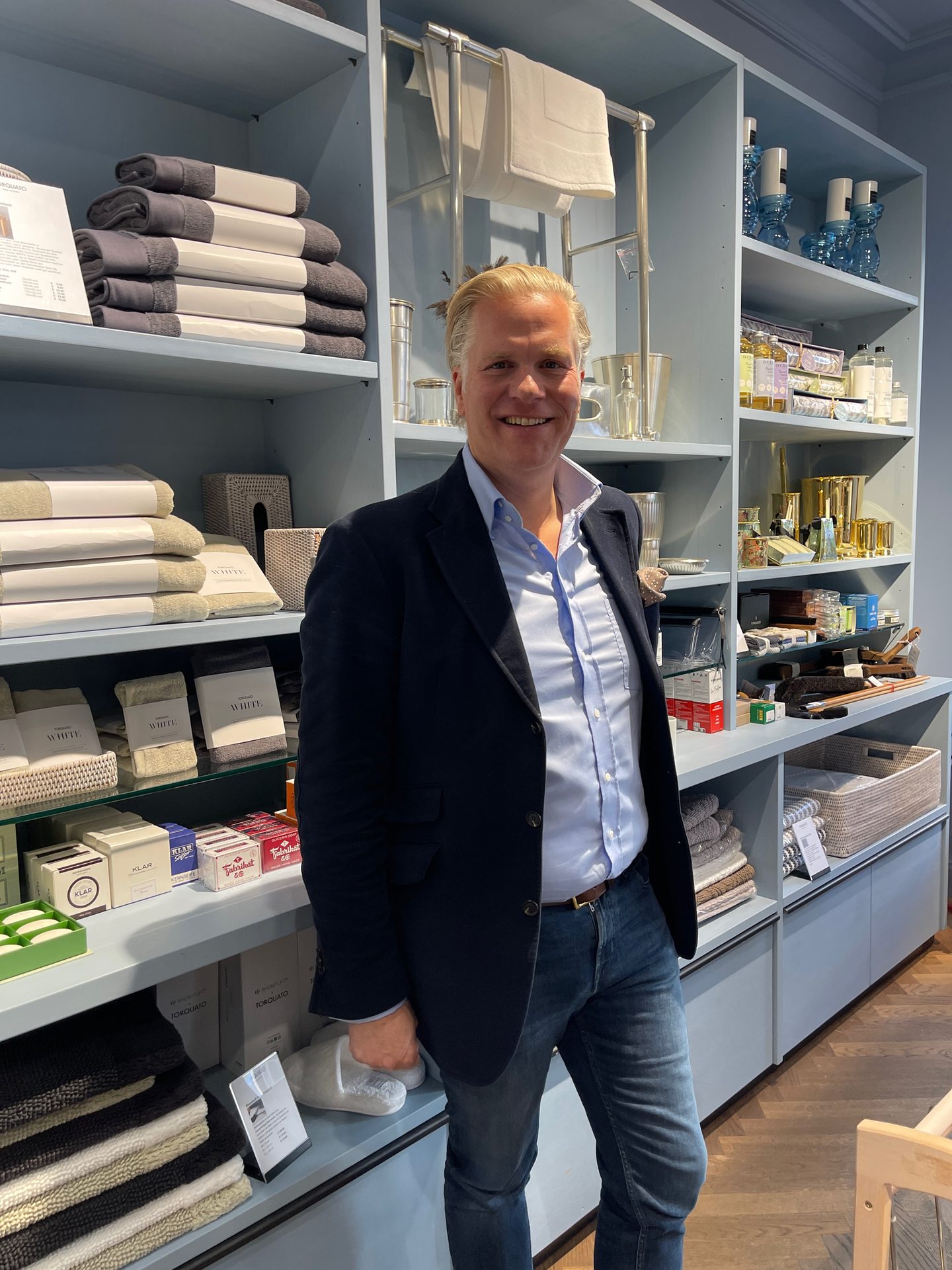 Smiling man in a home goods store with shelves full of towels, toiletries, and decor.