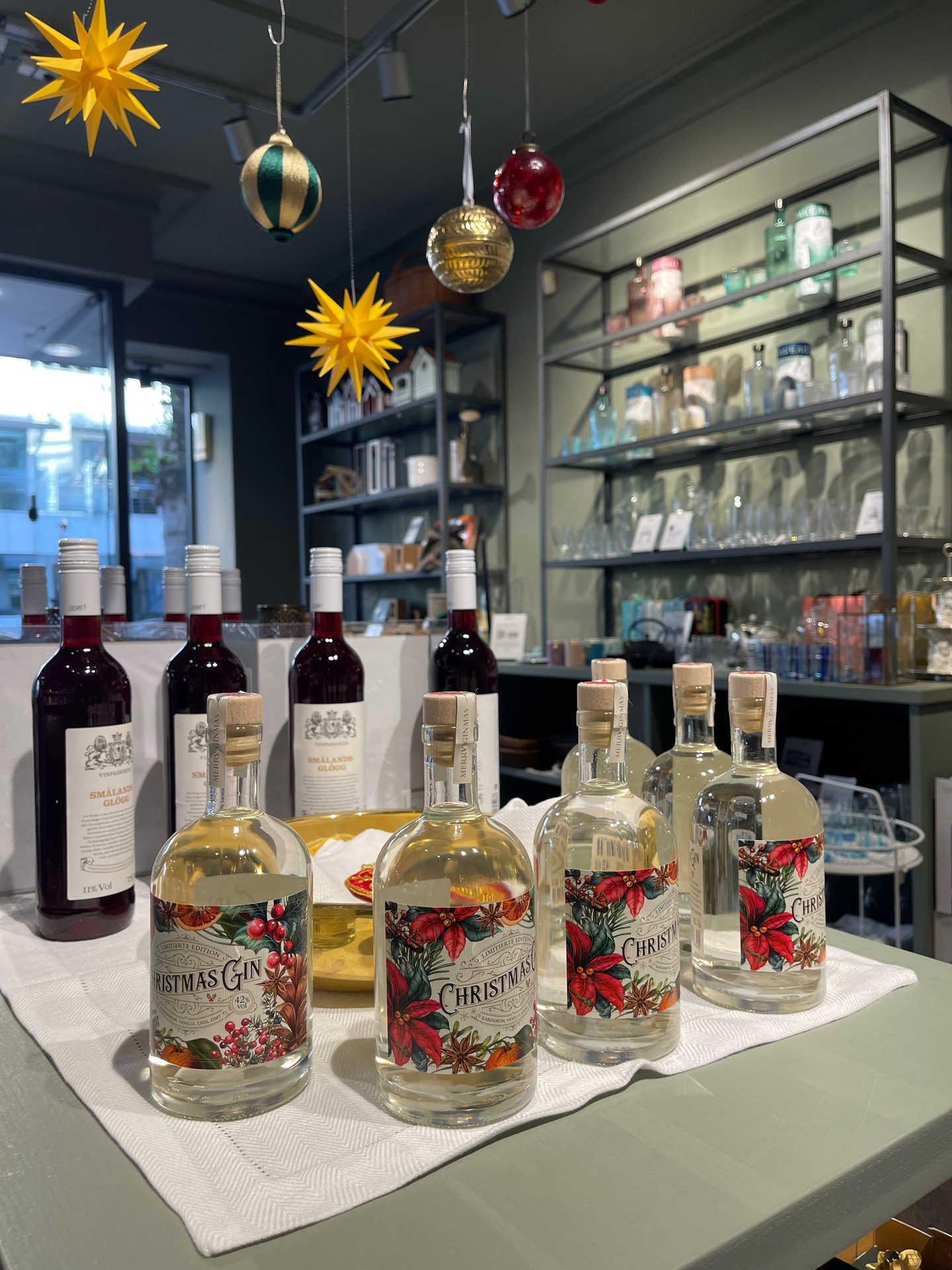 Christmas Gin & Glögg bottles displayed on a table with festive decorations and a glassware shelf.