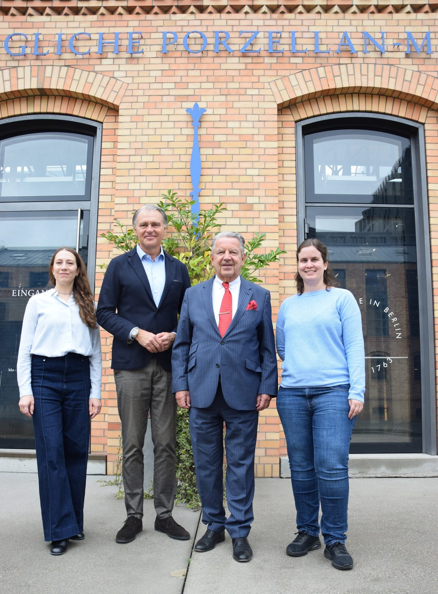 Four people, two men and two women, stand in front of a brick building with a blue "PORZELLAN" sign.