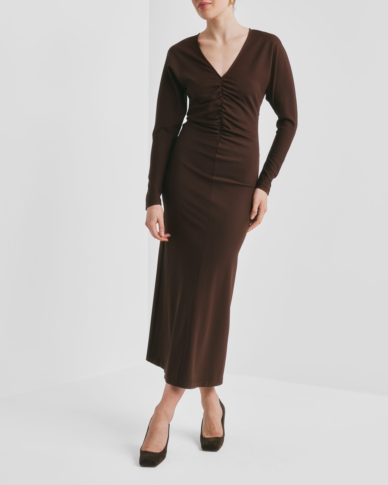 Woman in a brown long-sleeved ruched midi dress with a V-neck and dark brown pumps.