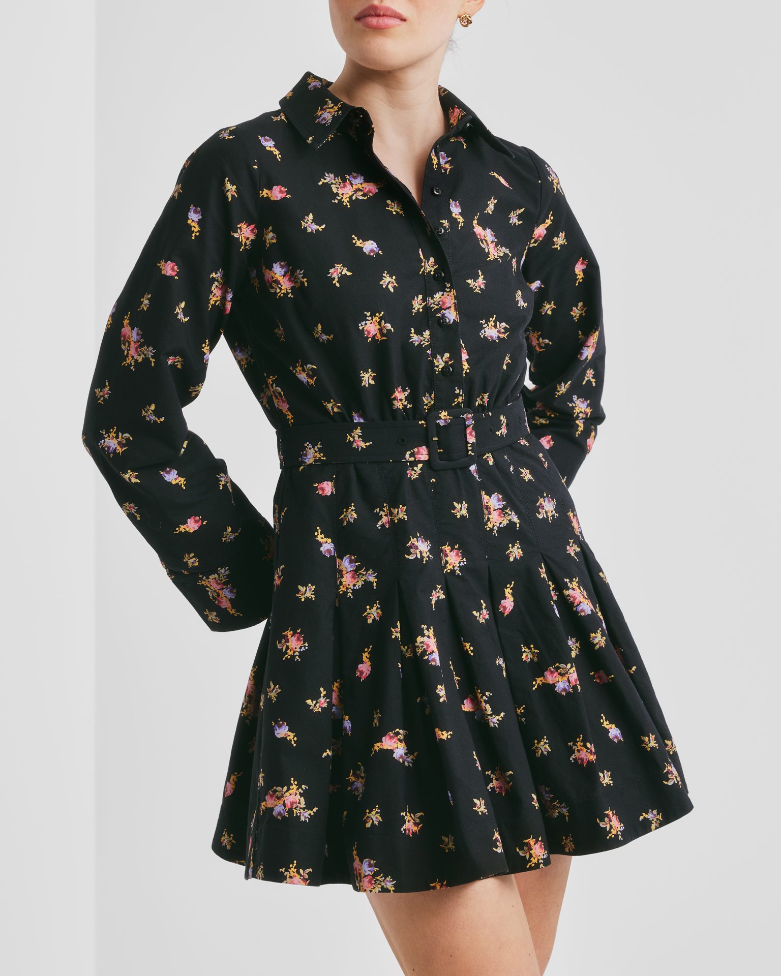 Woman wearing a black long-sleeved floral mini shirt dress with a belt.