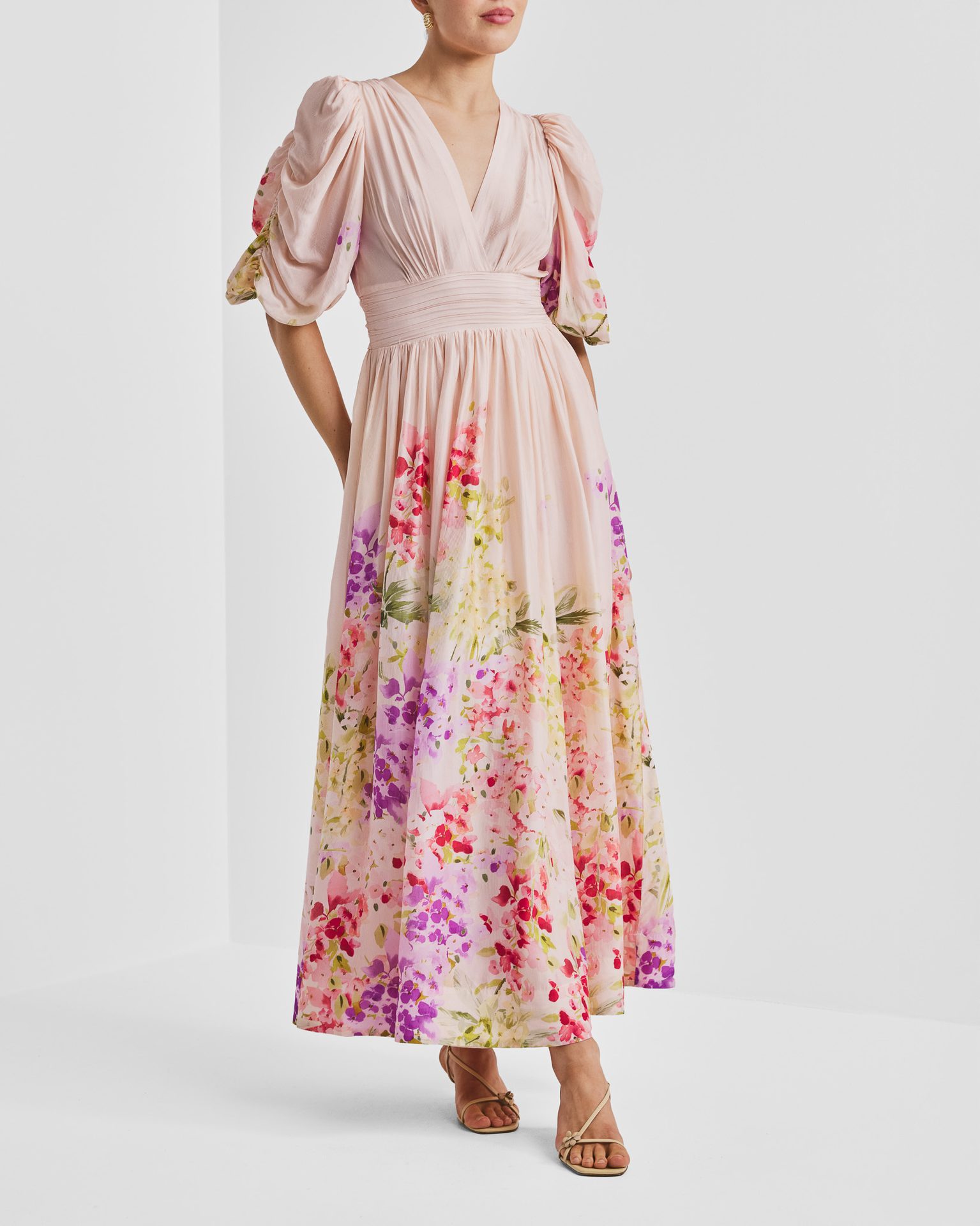 Woman in a pink floral midi dress with puffed sleeves and V-neck, standing.